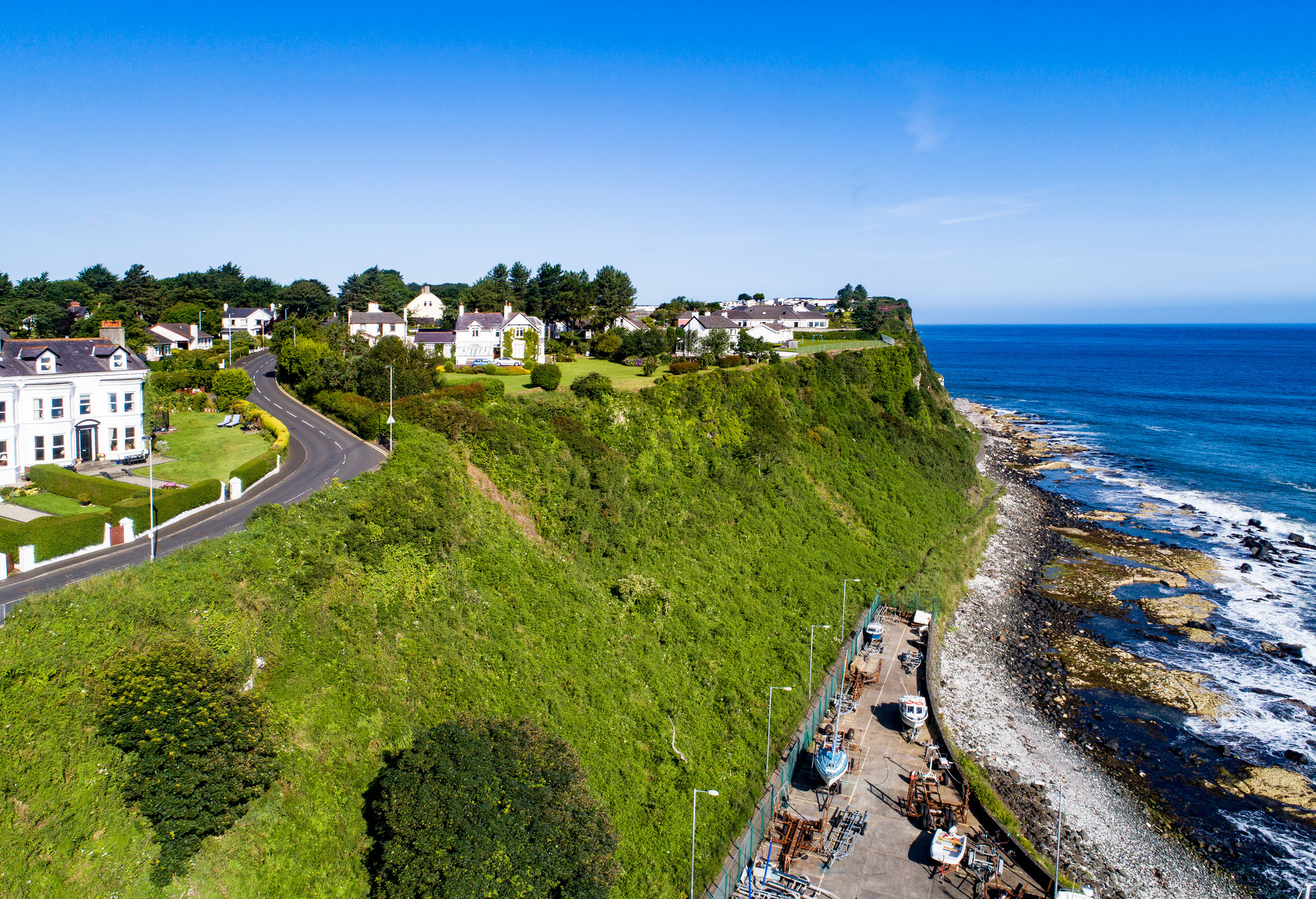 Atlantic coast with a steep cliff, marina and Causeway Coastal Road at Ballycastle, County Antrim, Northern Ireland, UK. Aerial view