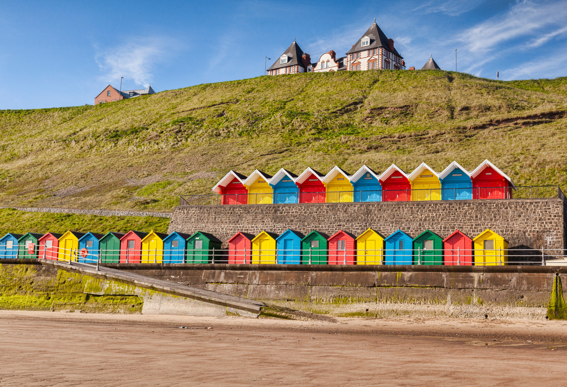 Rows of colorful beach huts on the promenade at Whitby Sands, Whitby, North Yorkshire, England, UK, on a beautiful sunny morning in spring.