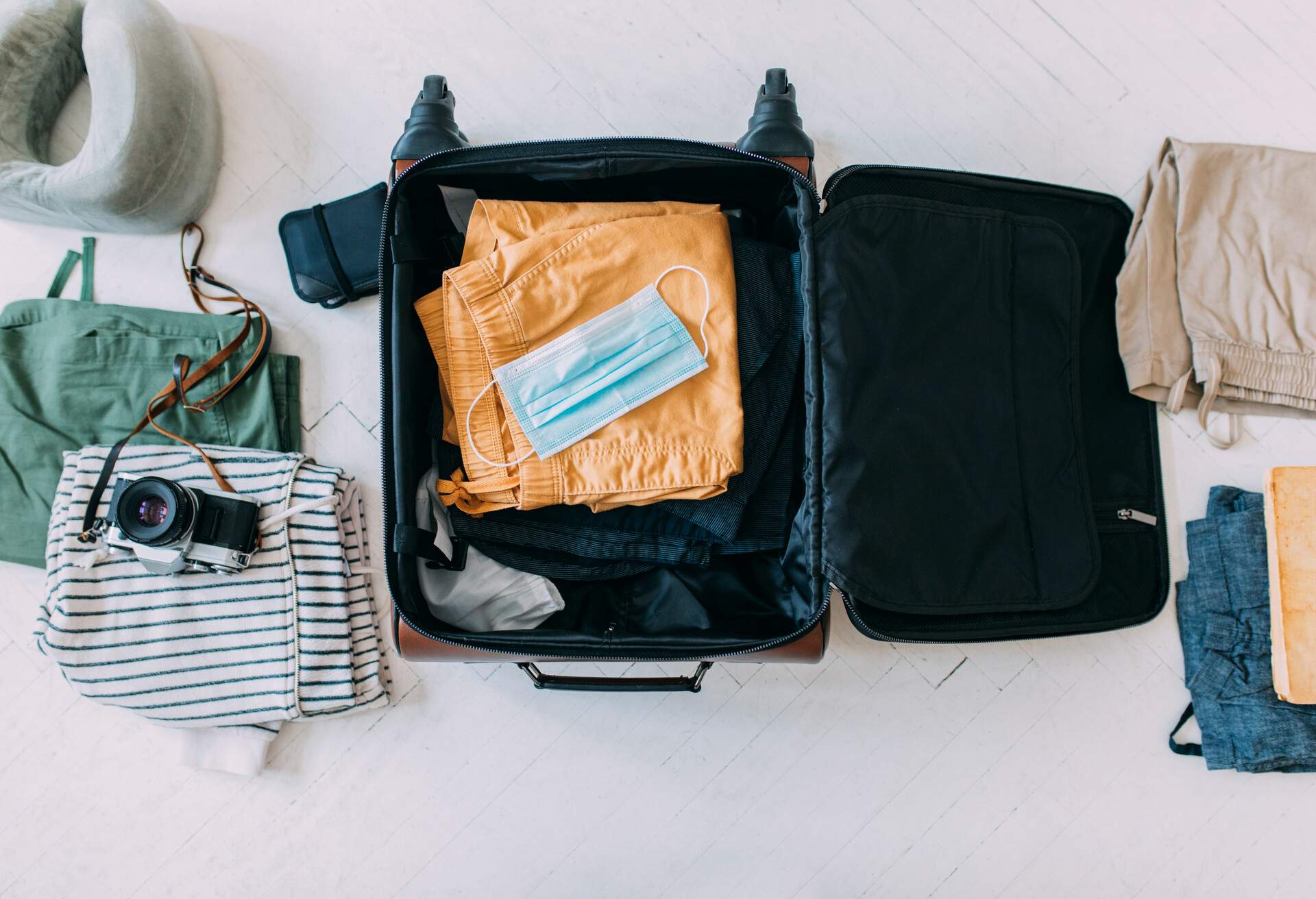 Protective face mask packed into a suitcase along with clothes and a camera, covid 19 prevention concept.