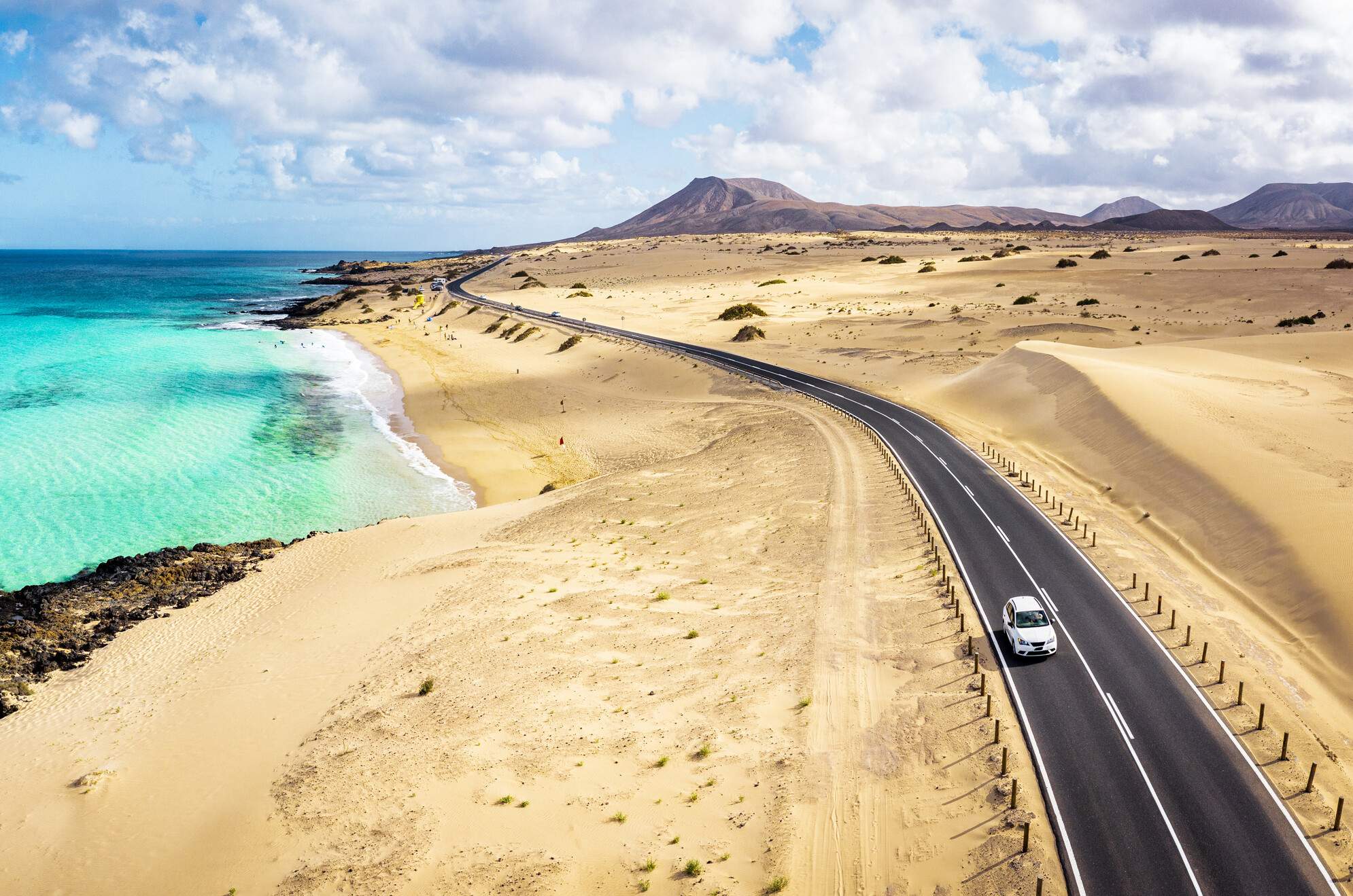 Aerial view of car driving on desert road by the turquoise sea, Corralejo Natural Park, Fuerteventura, Canary Islands, Spain