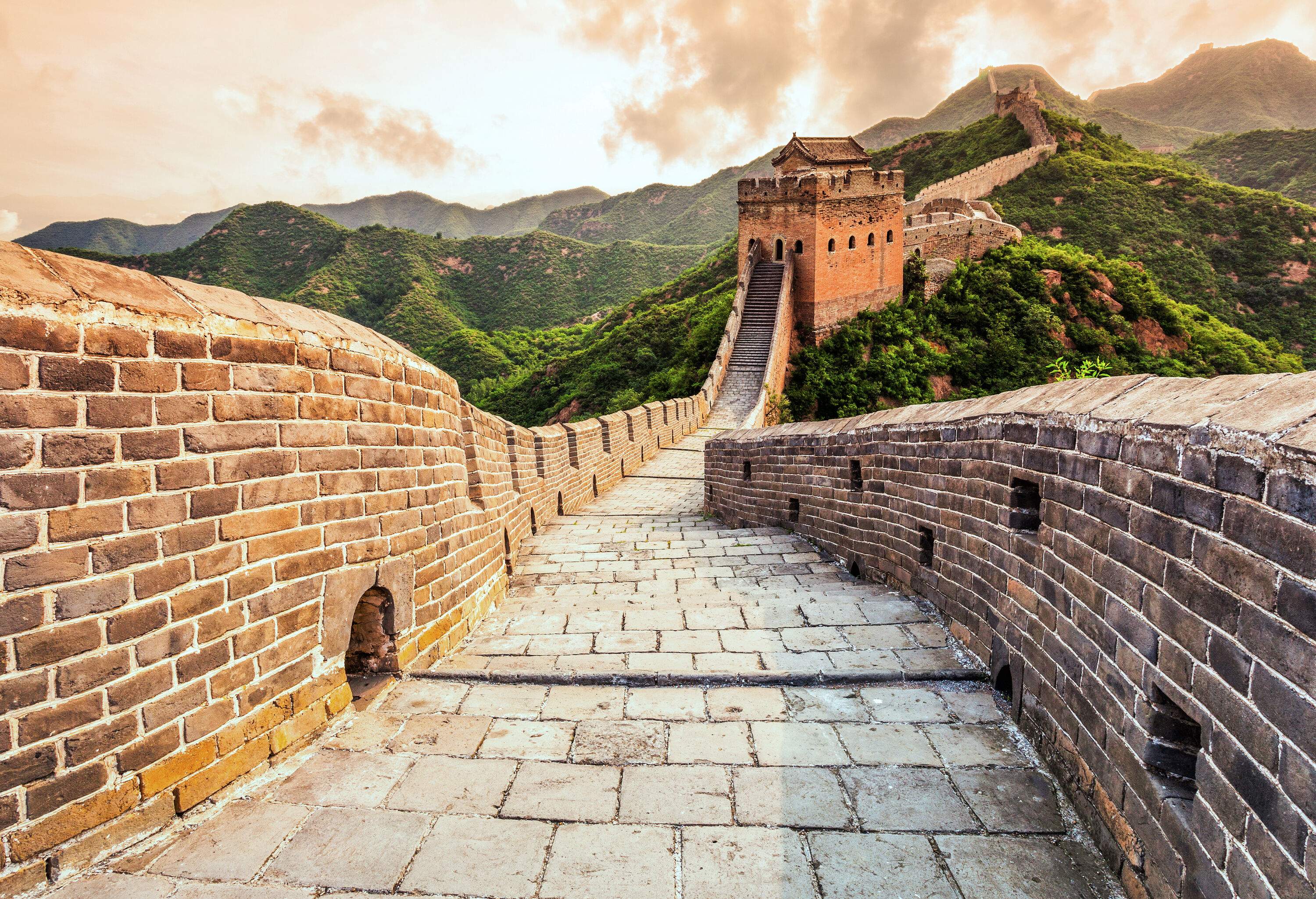 The majestic and historic Great Wall of China gracefully winds through lush foliage captured during the scenic sunset.