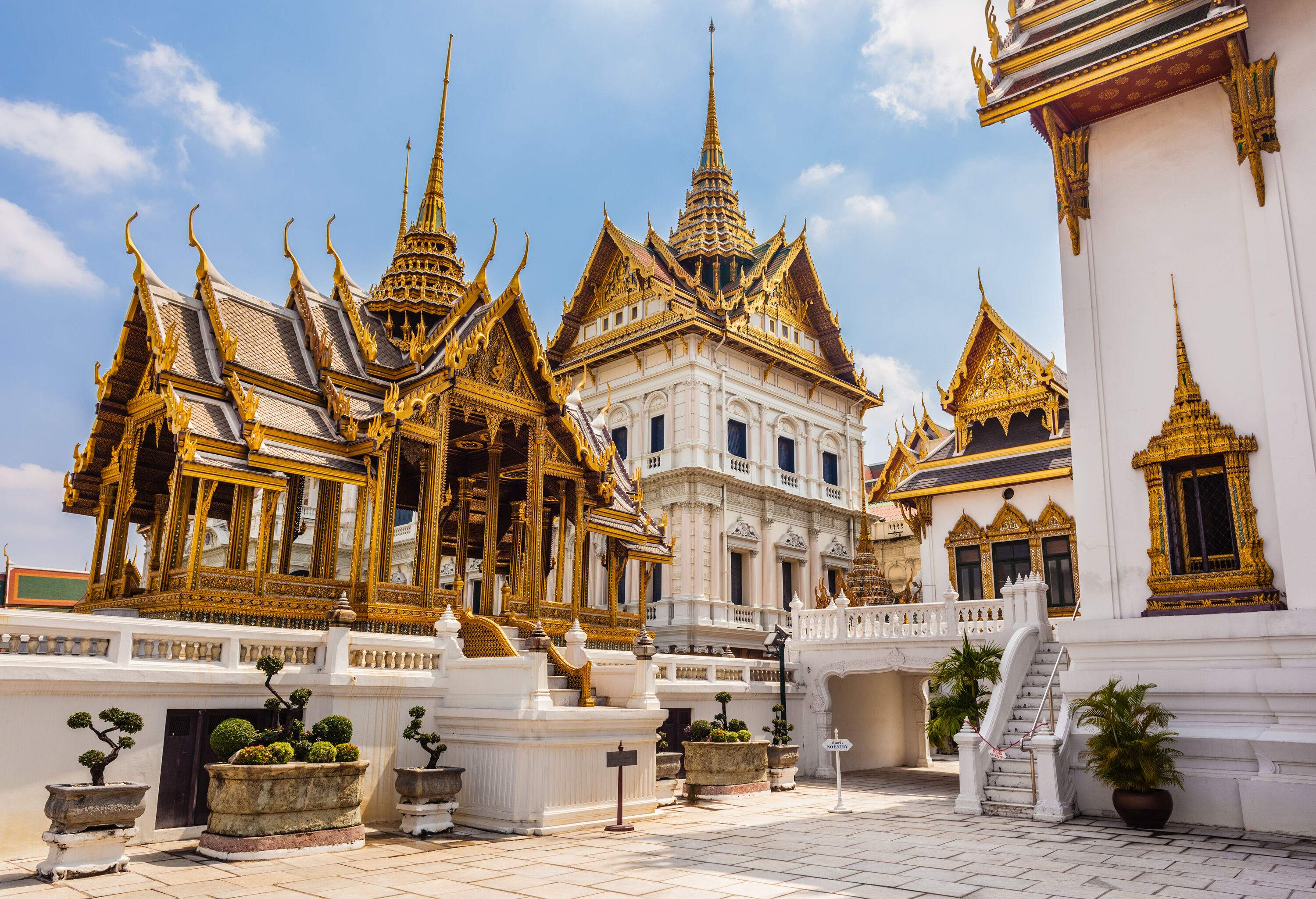 A golden bell-shaped stupa is perched atop Phra Thinang Dusit Maha Prasat, a white temple that is exquisitely constructed with stepped-out roofs covered in gold and sharp finials.