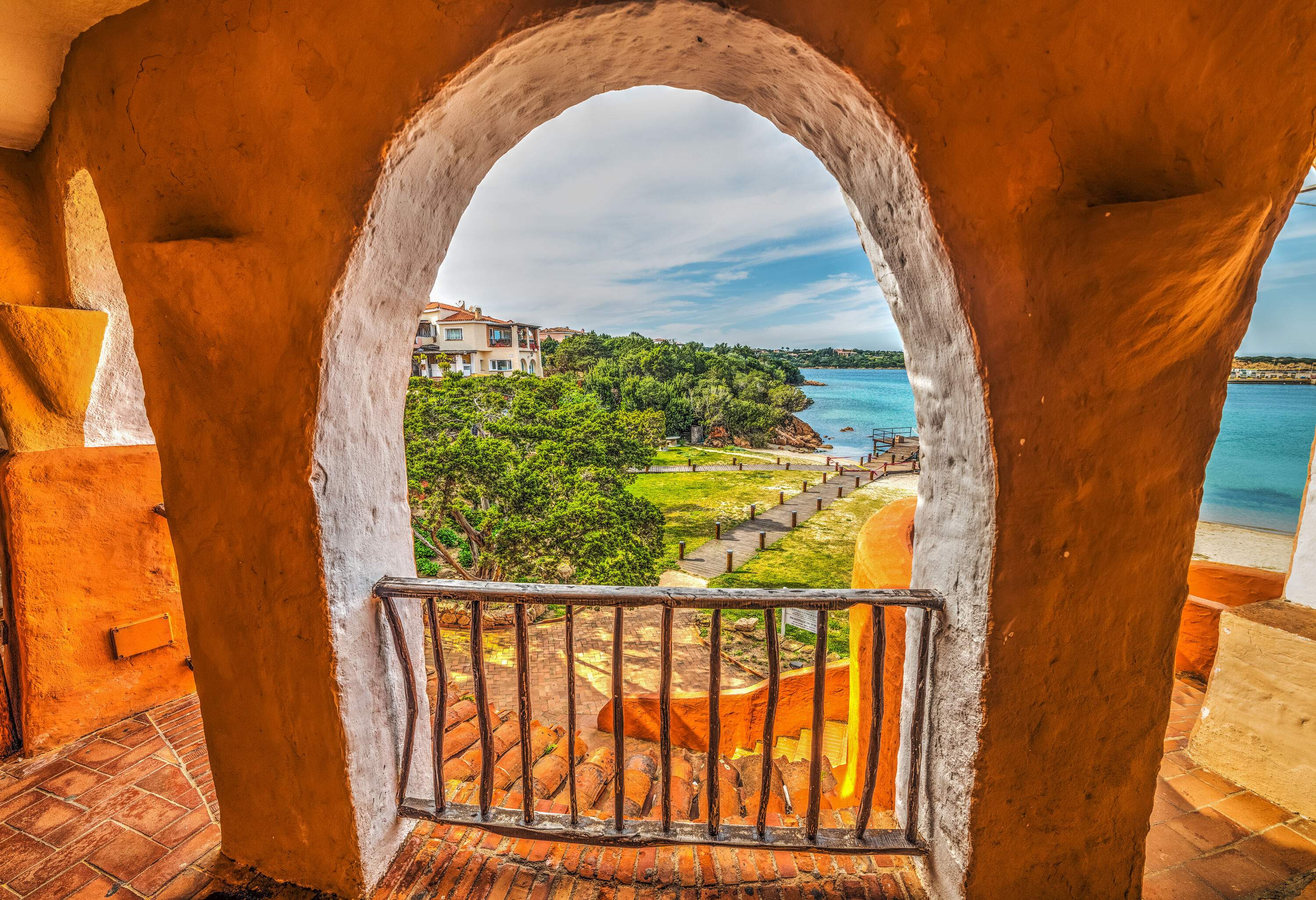 A rustic stucco arch with views of a boardwalk that leads down to the beach.