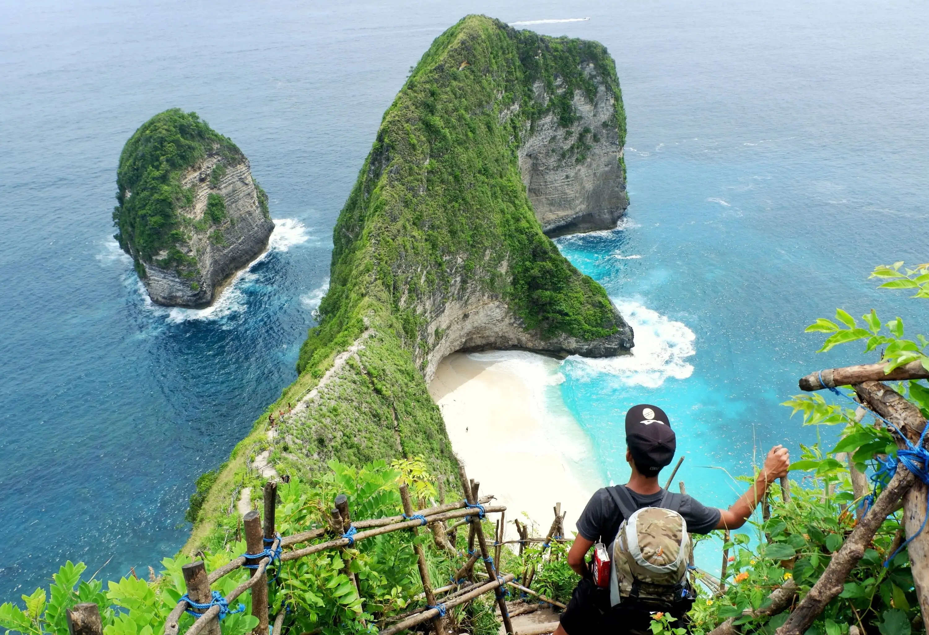 A man staring out over the bluff and the azure sea from atop a ladder in the mountains.
