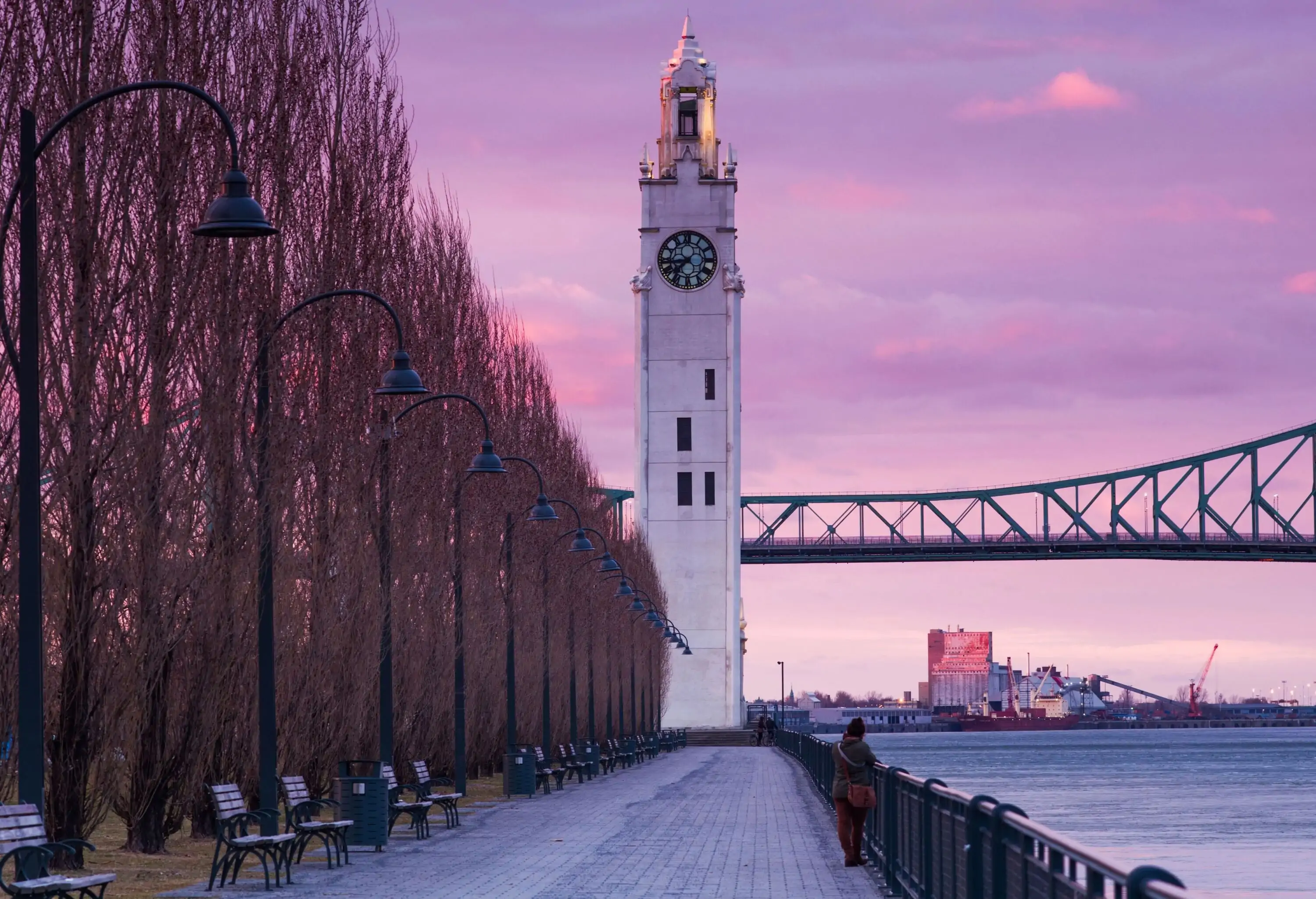 A woman standing on a promenade with the Old Port Clock Tower in the background. 