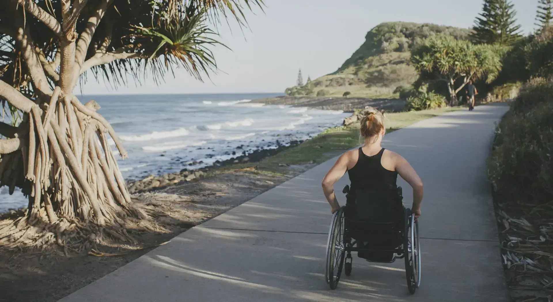 A person in a wheelchair on a sidecalk next to the sea