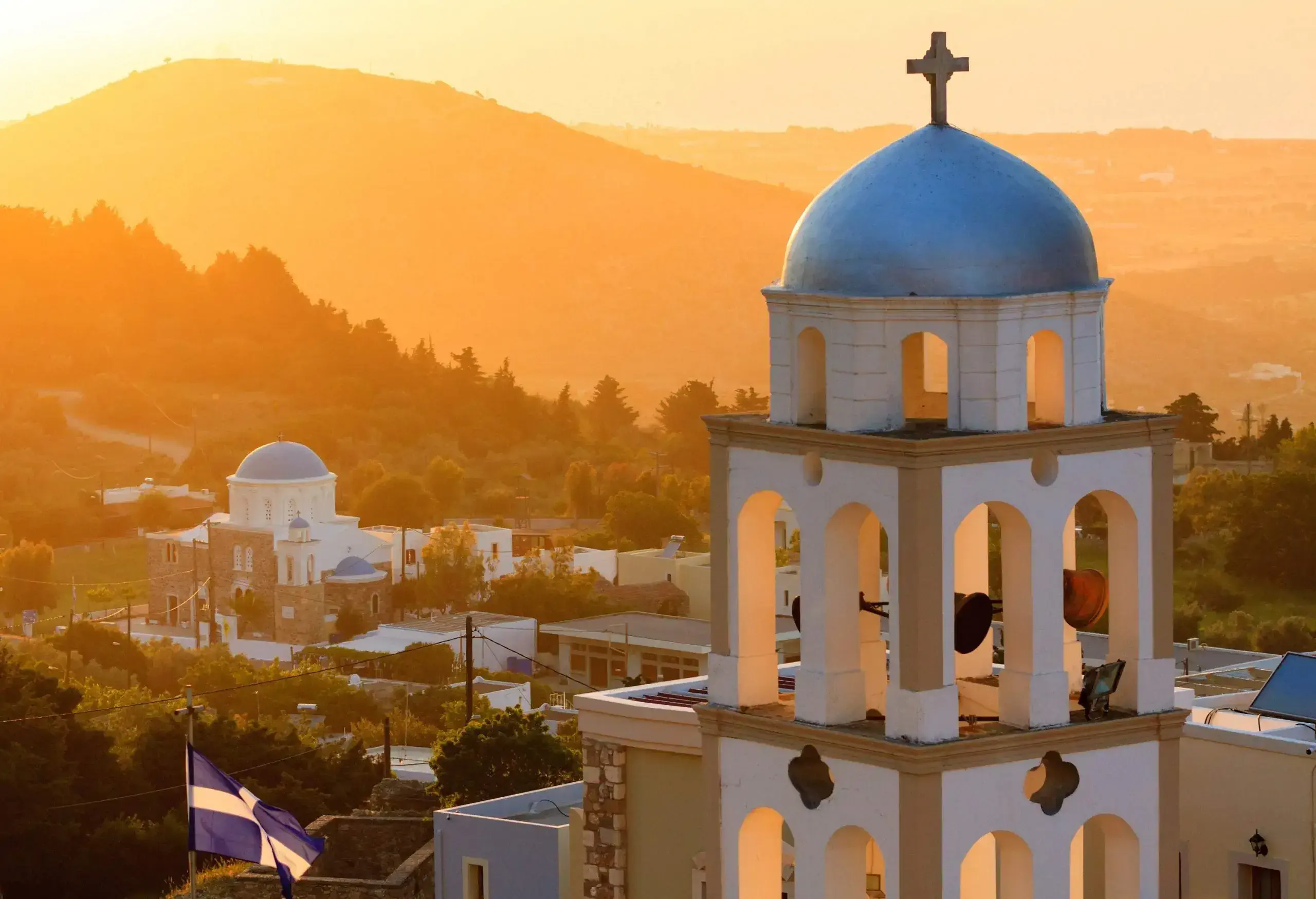 A church belfry overlooking its neighbouring houses and a mountain.