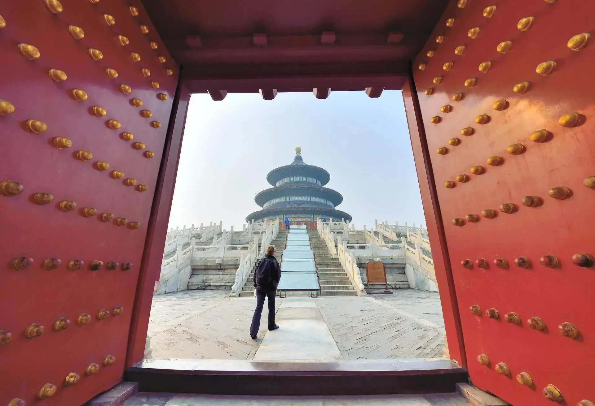 A man wearing dark winter clothing the Forbidden City, on a clear sky day