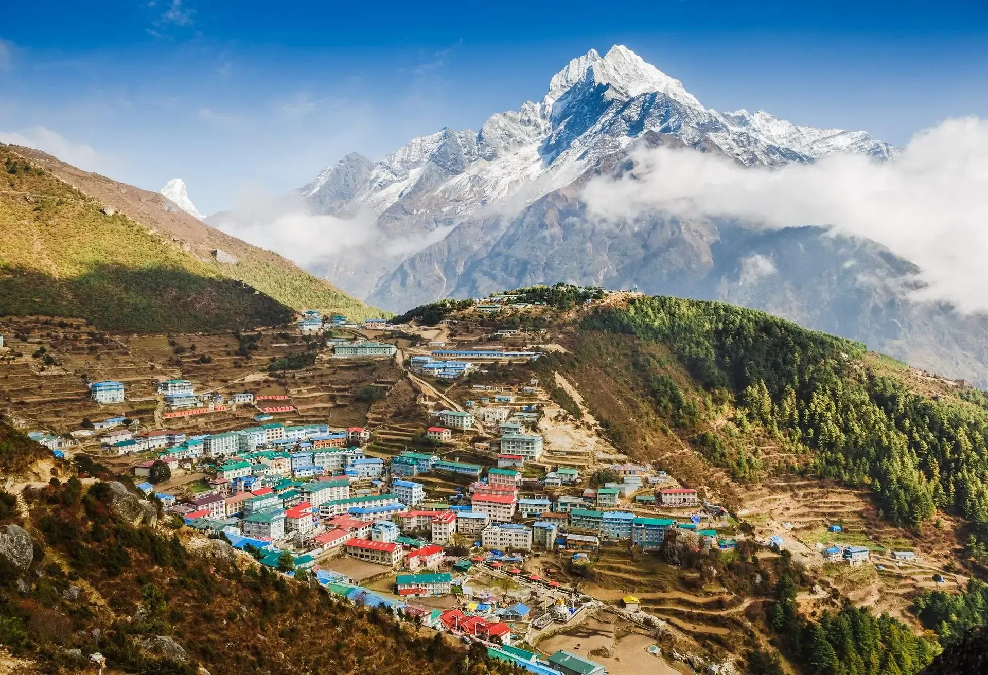 Colourful buildings between the hills with snow-covered mountains in the background.