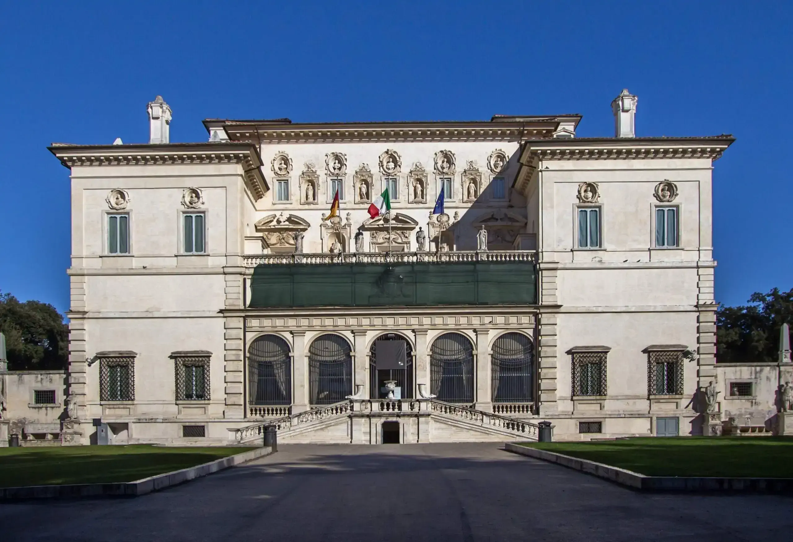 Galleria Borghese is an art gallery with a grand front staircase, arch windows, and intricately carved façade between two square buildings.