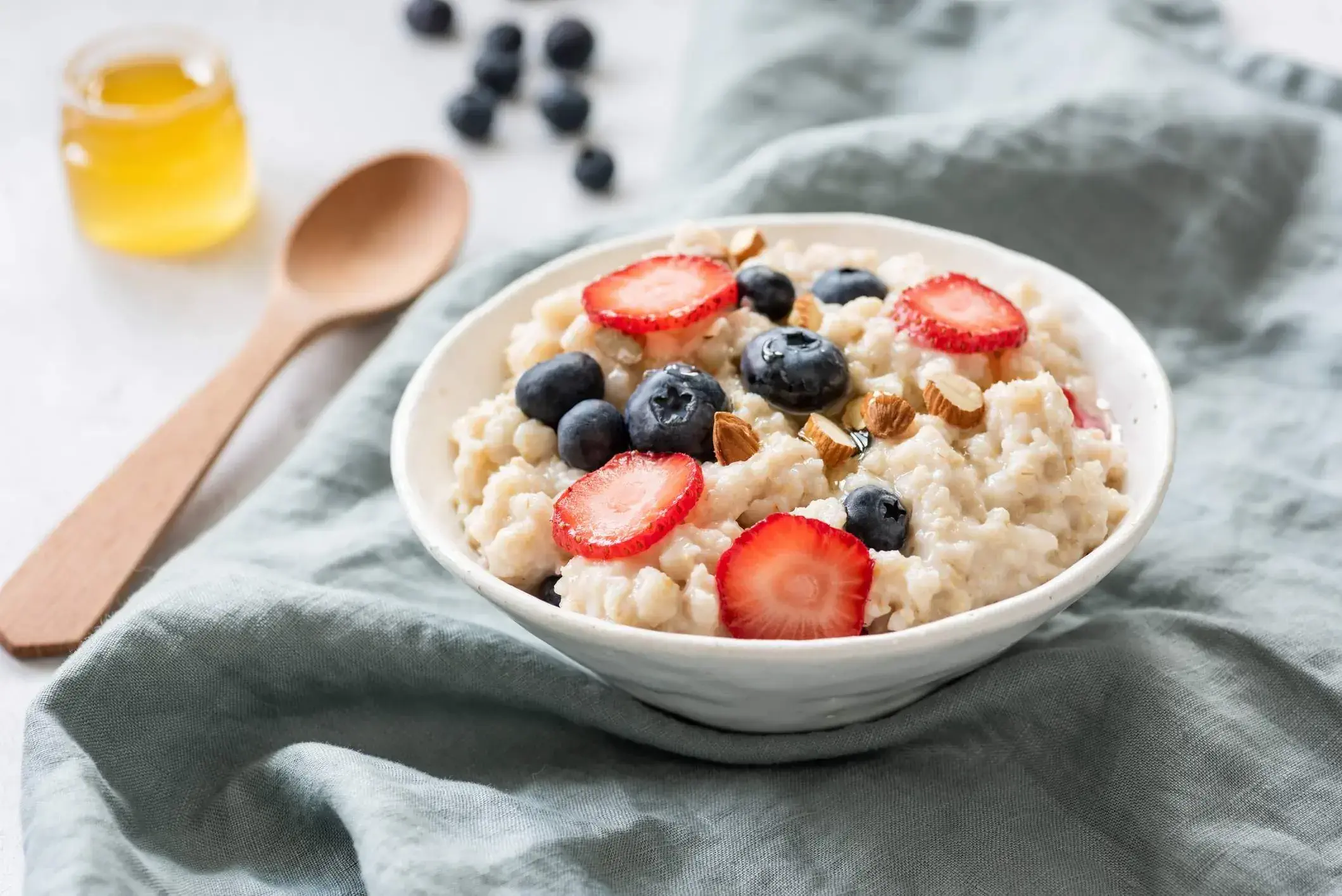white bowl with porridge and fruit, wooden spoon on a grey fabric napkin