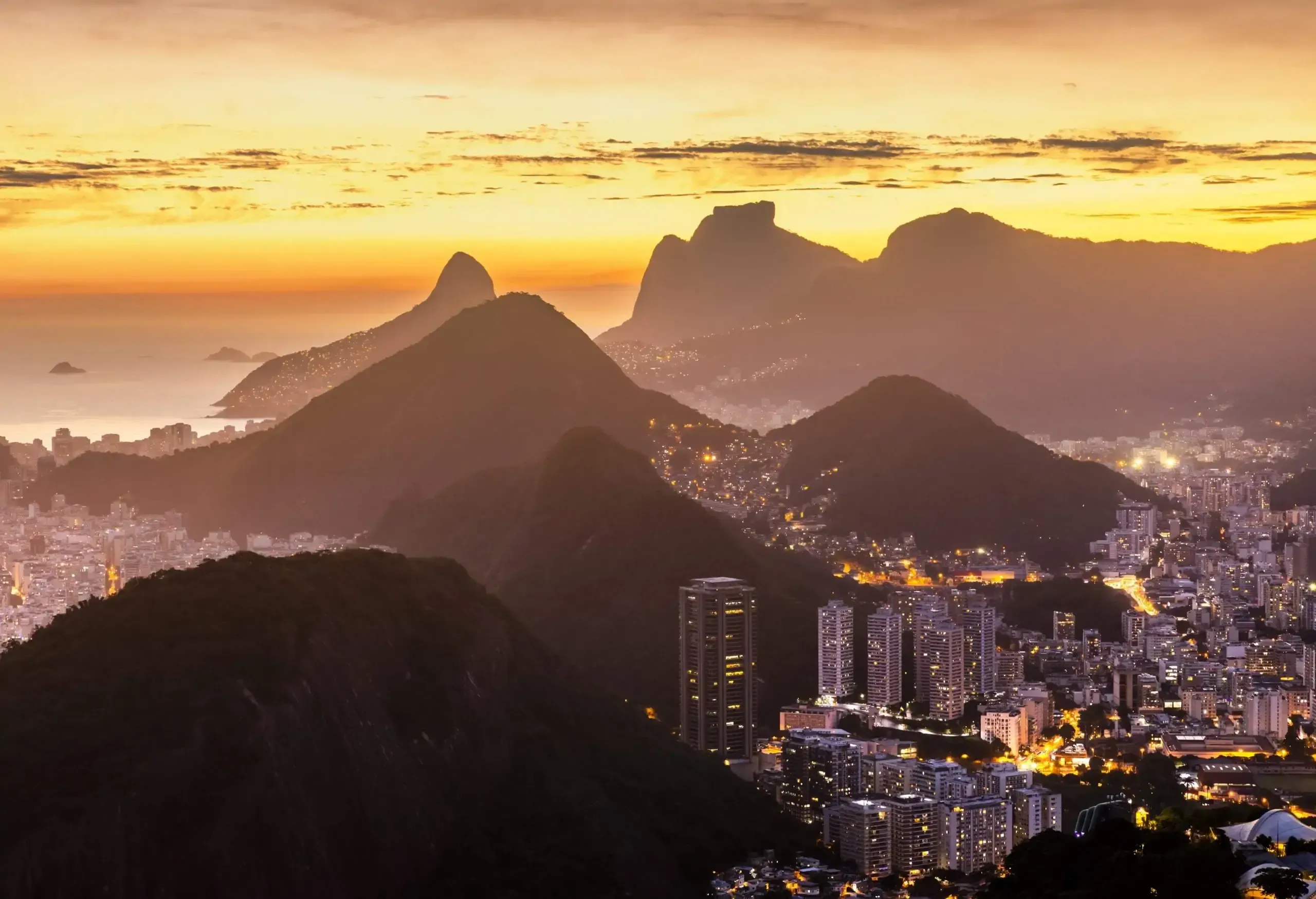 High angle view of large coast city at sunset, tall lit buildings between mountans