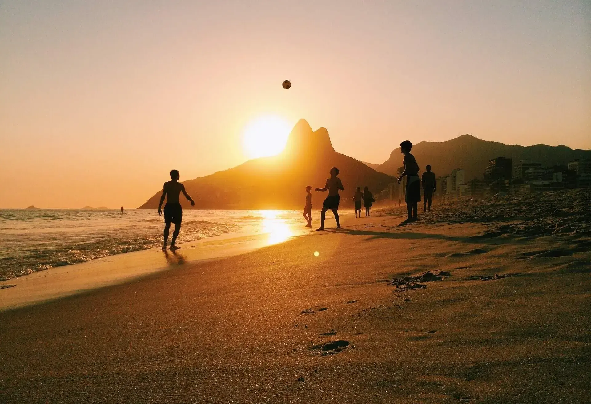 Silhouette of children playing football at sunset on Ipanema beach with mountains in the background