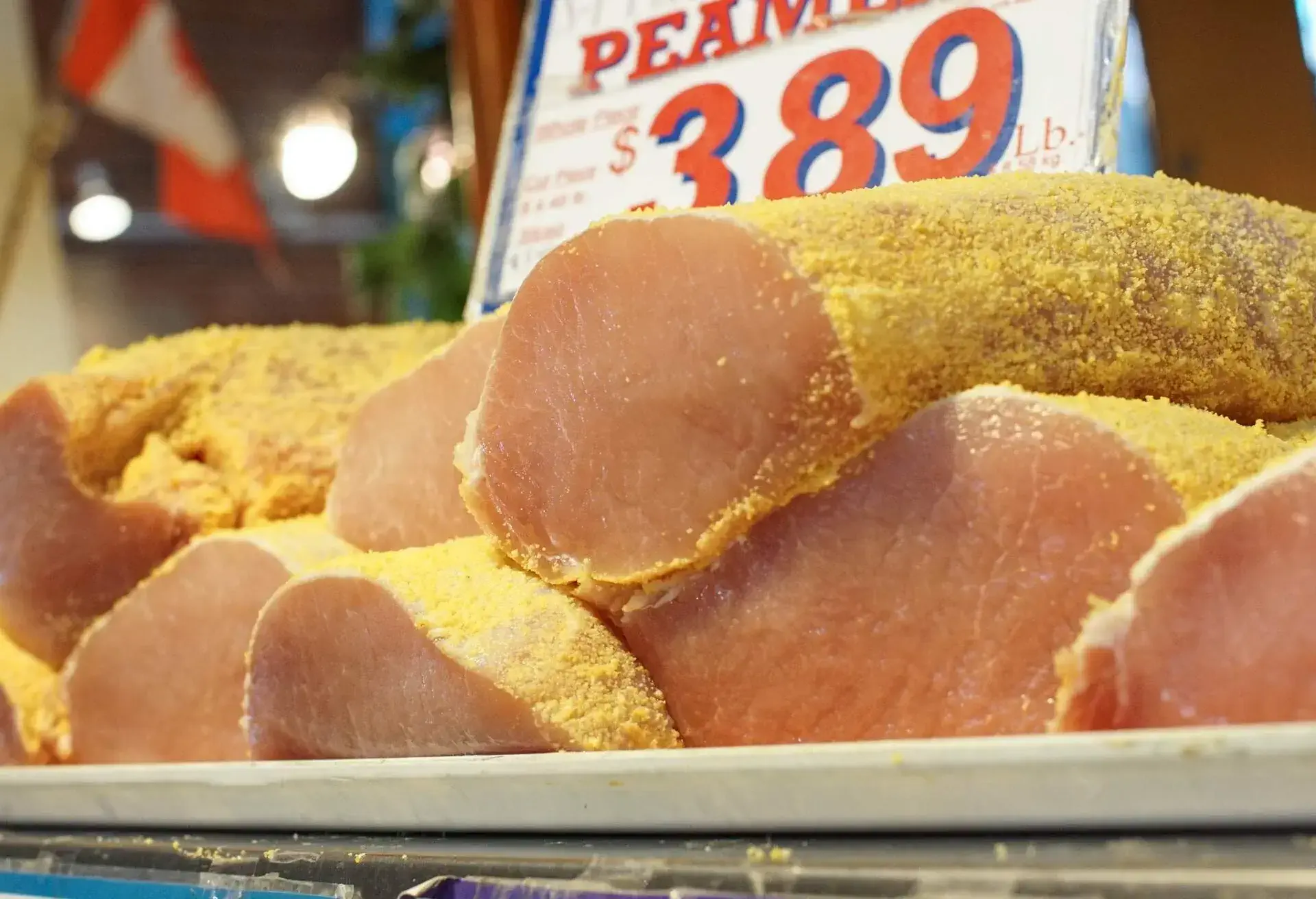 Peameal Bacon pieces on a white platter with a price sign behind
