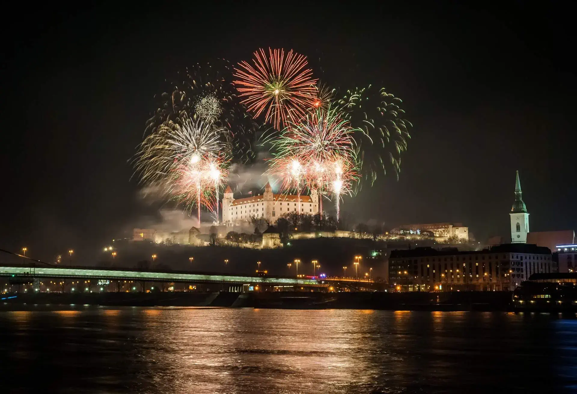A riverview at night with fireworks and a castle in the middle 