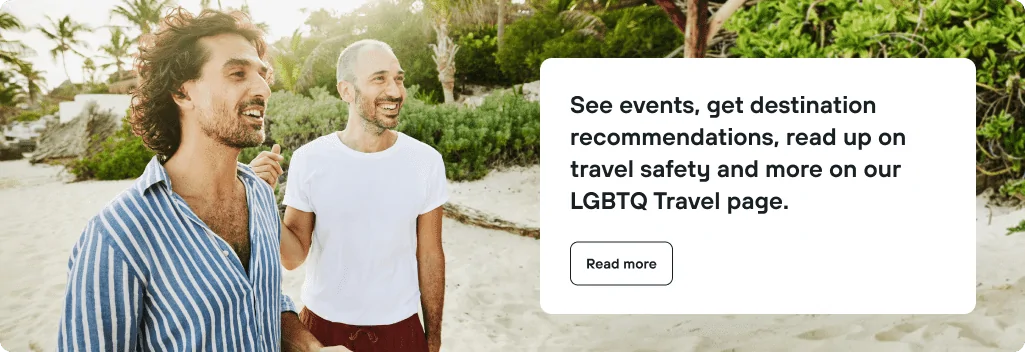 Two individuals stand on a sandy beach surrounded by palm trees, engaged in conversation. Text box highlights LGBTQ travel resources.