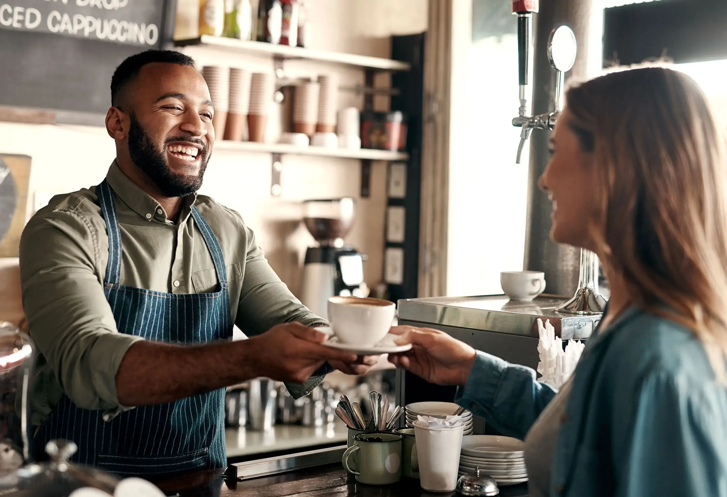 A joyful barista serves a cup of coffee to his female customer.