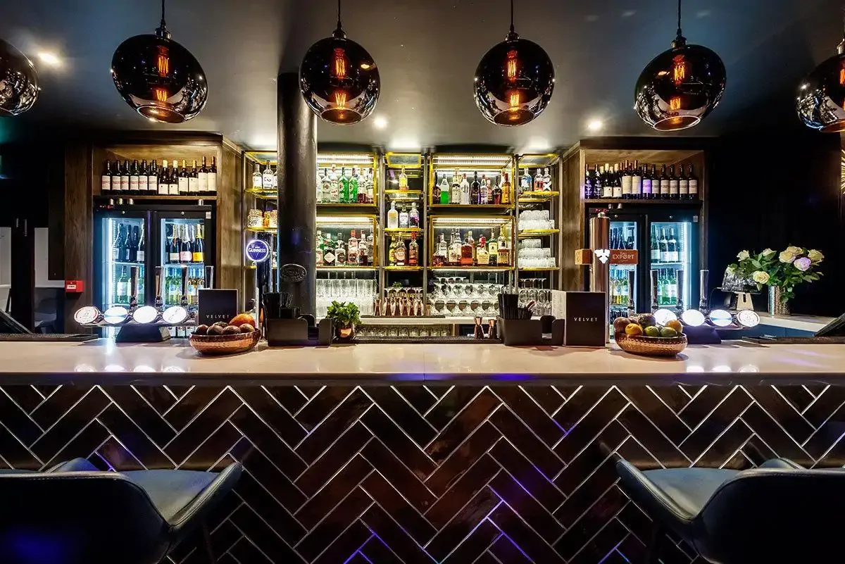 A stylish hotel bar with a sleek modern design, illuminated liquor shelves, and elegant pendant lighting.