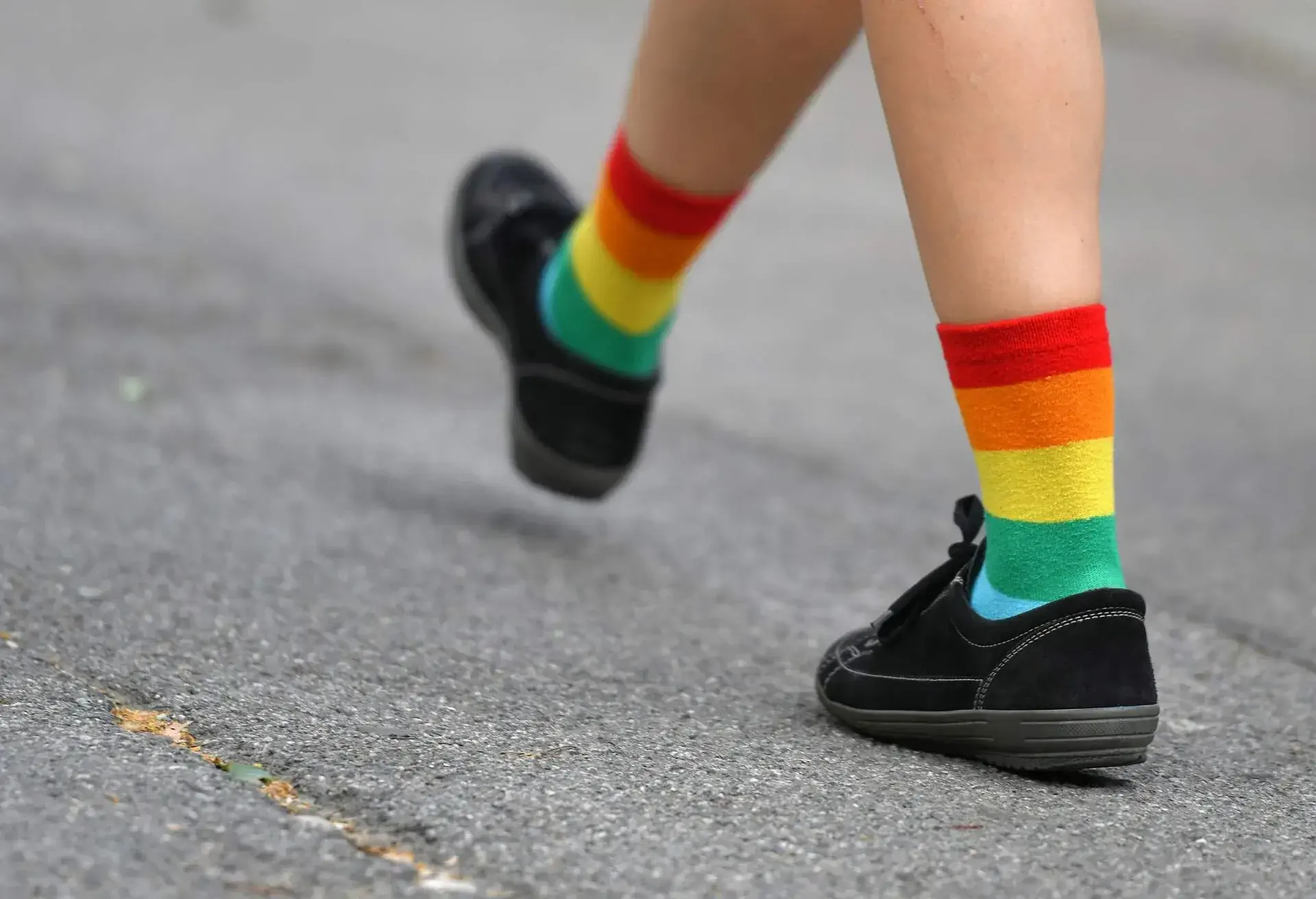 A person in black shoes and colourful socks walks down a street.