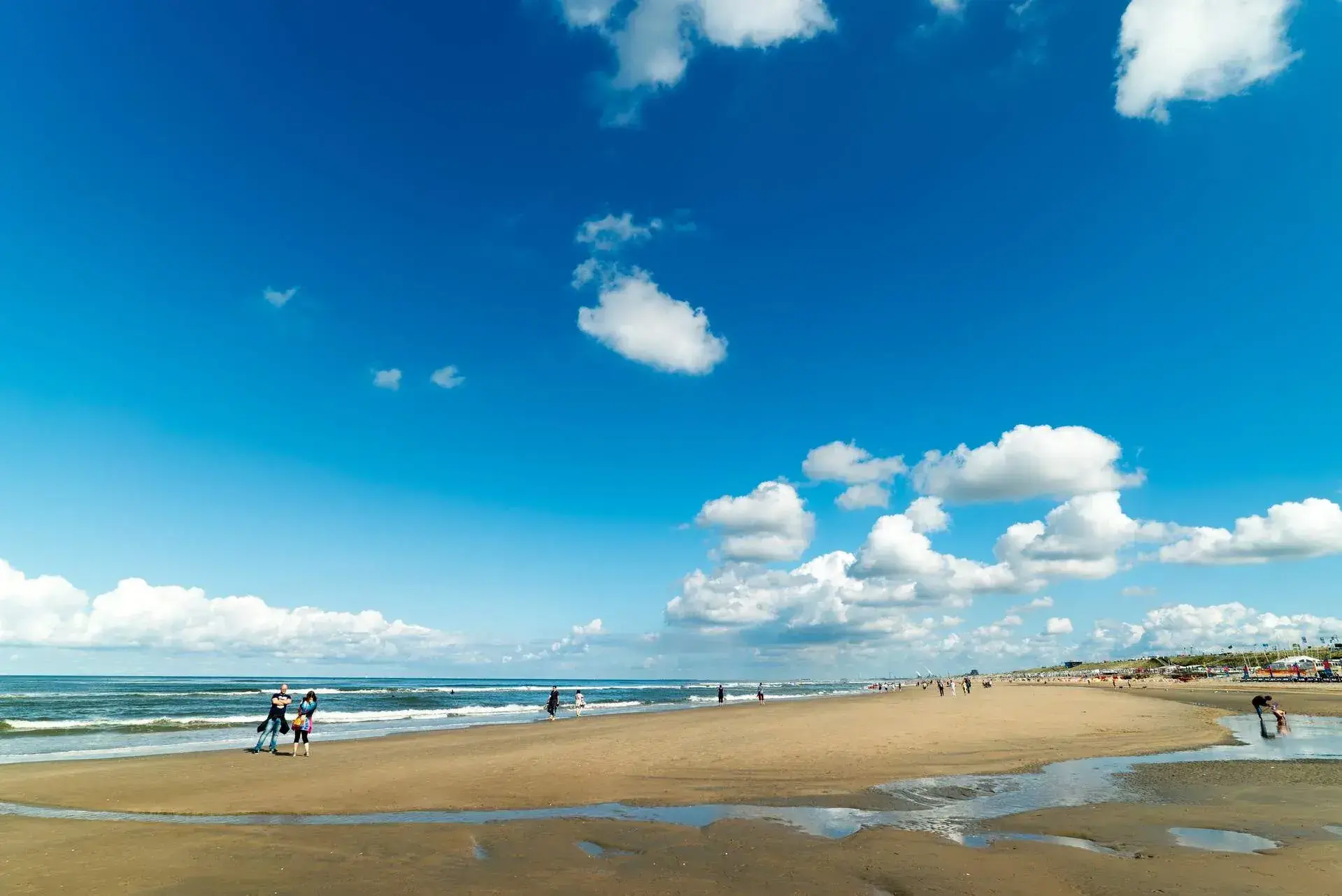People stroll on a beach with gentle waves.
