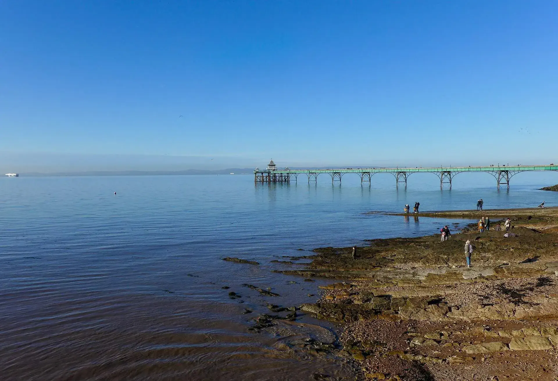A long and old pier on the coast and some people walking on the seaside