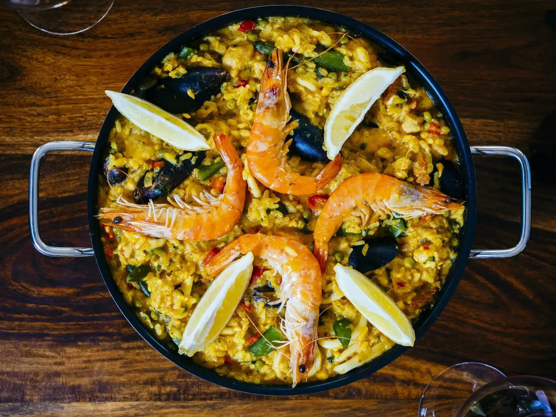 A dish with seasoned steamed rice topped with shrimps, mussels, and lemon slices.