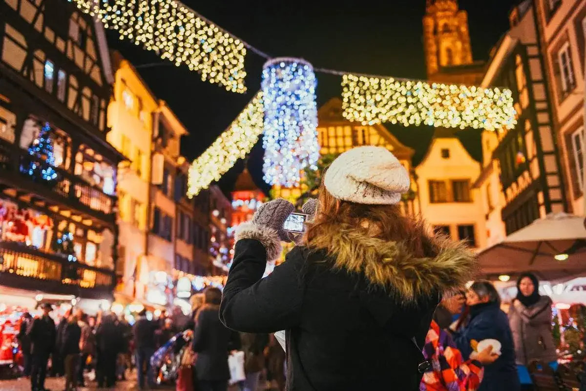 A woman dressed in winter clothes takes a photo at a French Christmas market
