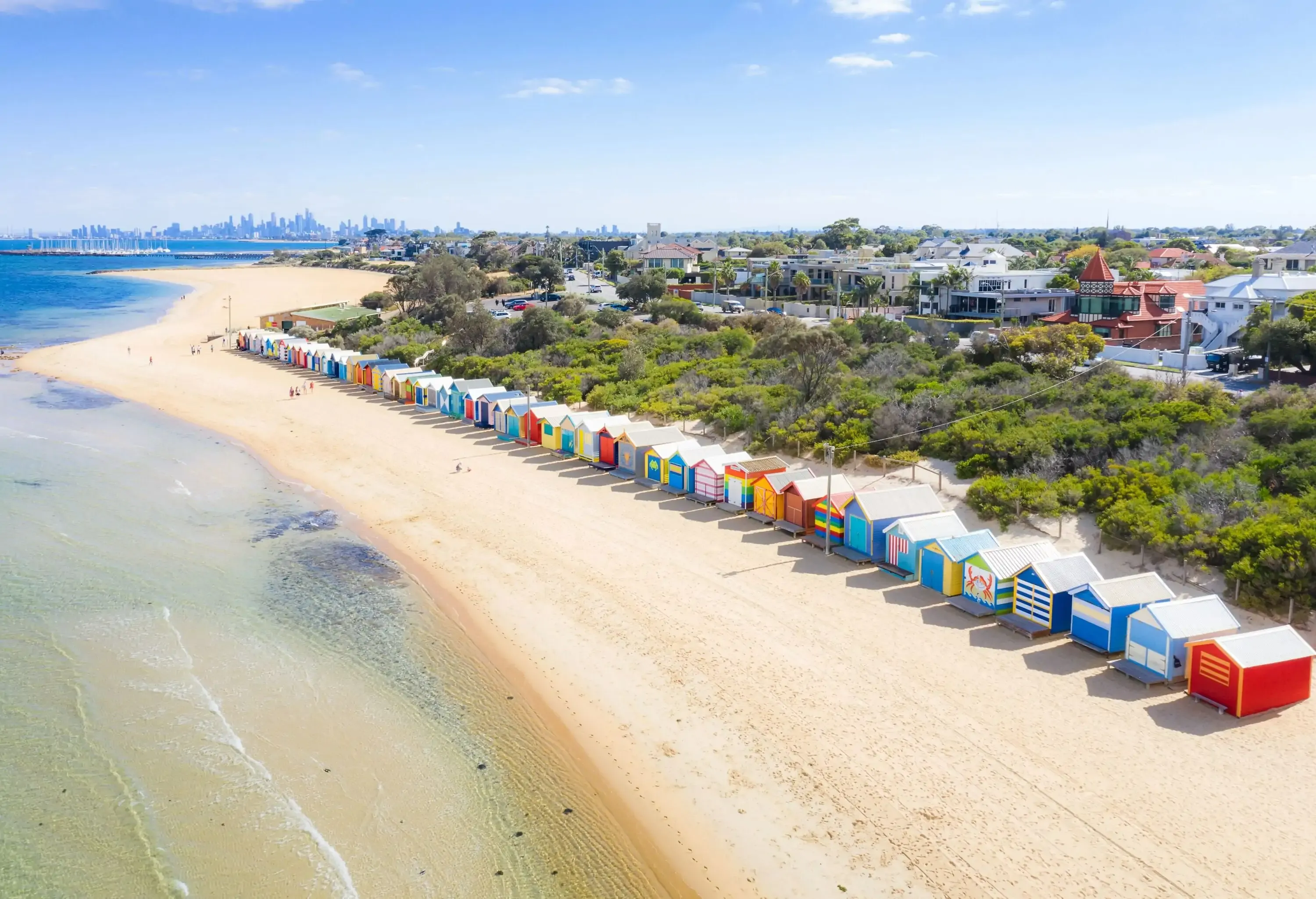 Aerial view of colorful Brighton Bathing Boxes on white sandy beach at Brighton beach with city in background in Melbourne, Victoria, Australia
