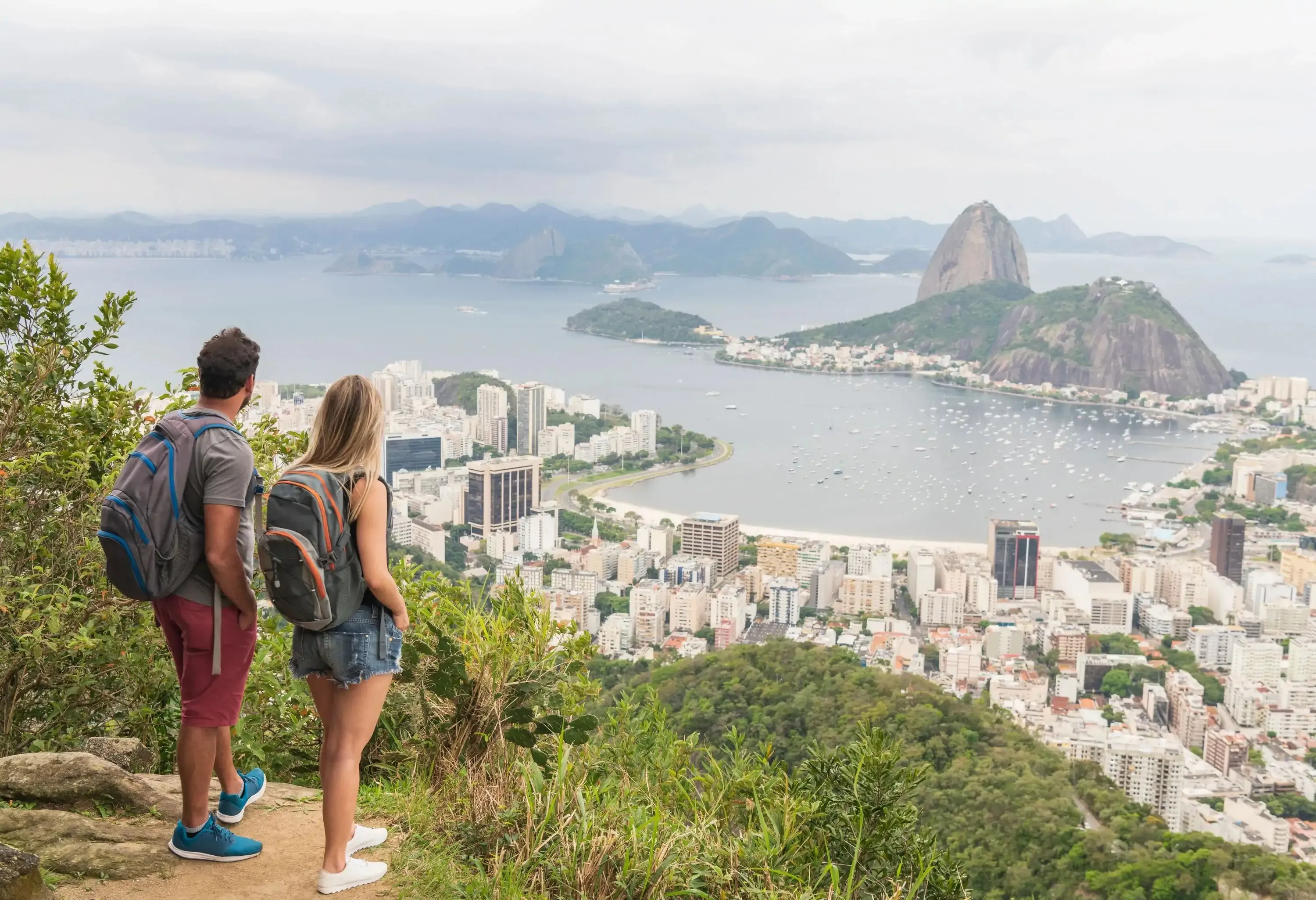 Backpacking tourists standing with views of Sugar Loaf Mountain in Rio de Janeiro, boyfriend and girlfriend backpackers with rucksacks, looking at view