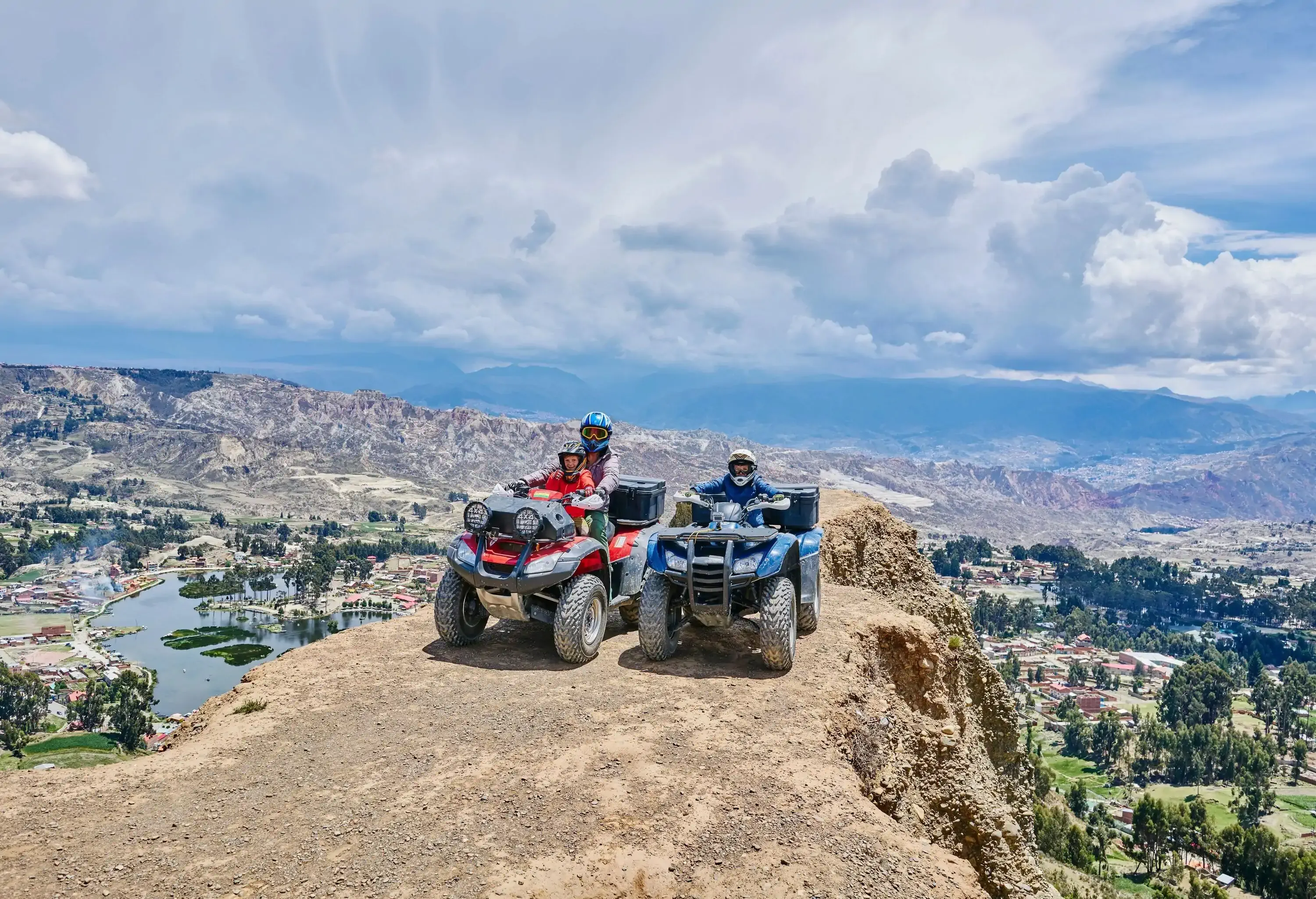 Riders on two quadbikes pose for a photo at the edge of a cliff with overlooking views of a wide landscape.