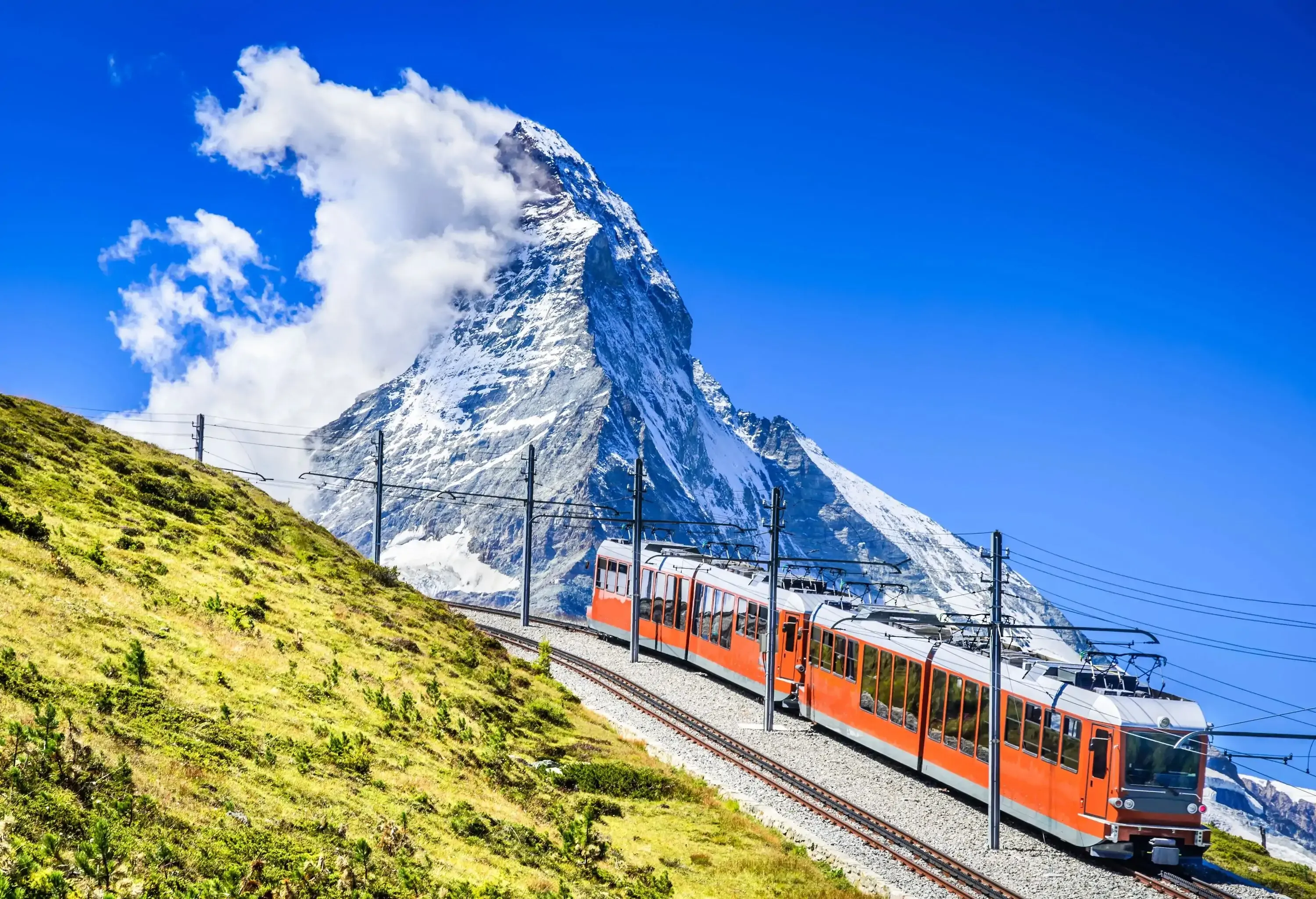 A mountain rack train smoothly descends the slopes, as a cloud-covered glacier mountain top serves as a stunning background in the distance.