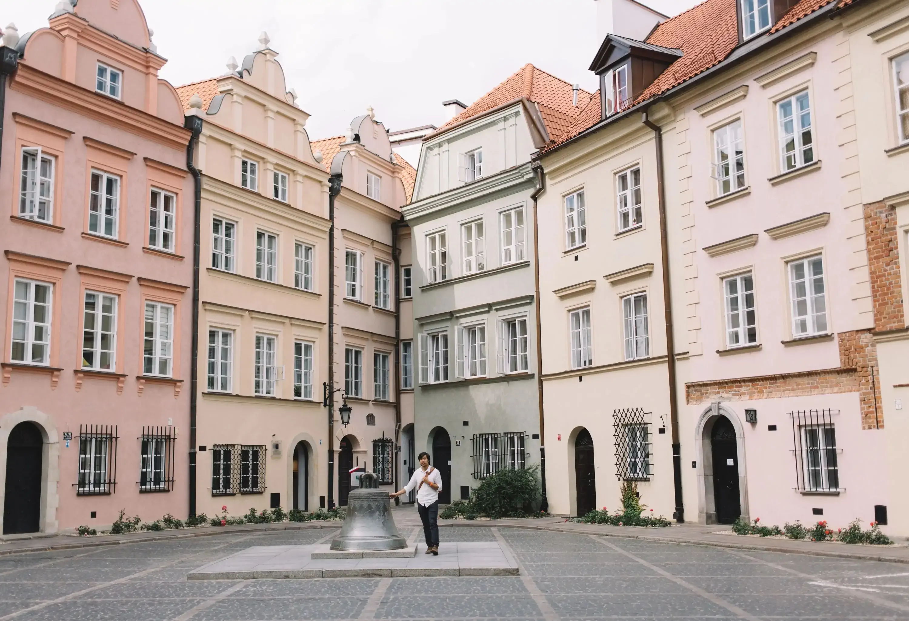A man touches a big bell in the middle of a courtyard surrounded by tall buildings.