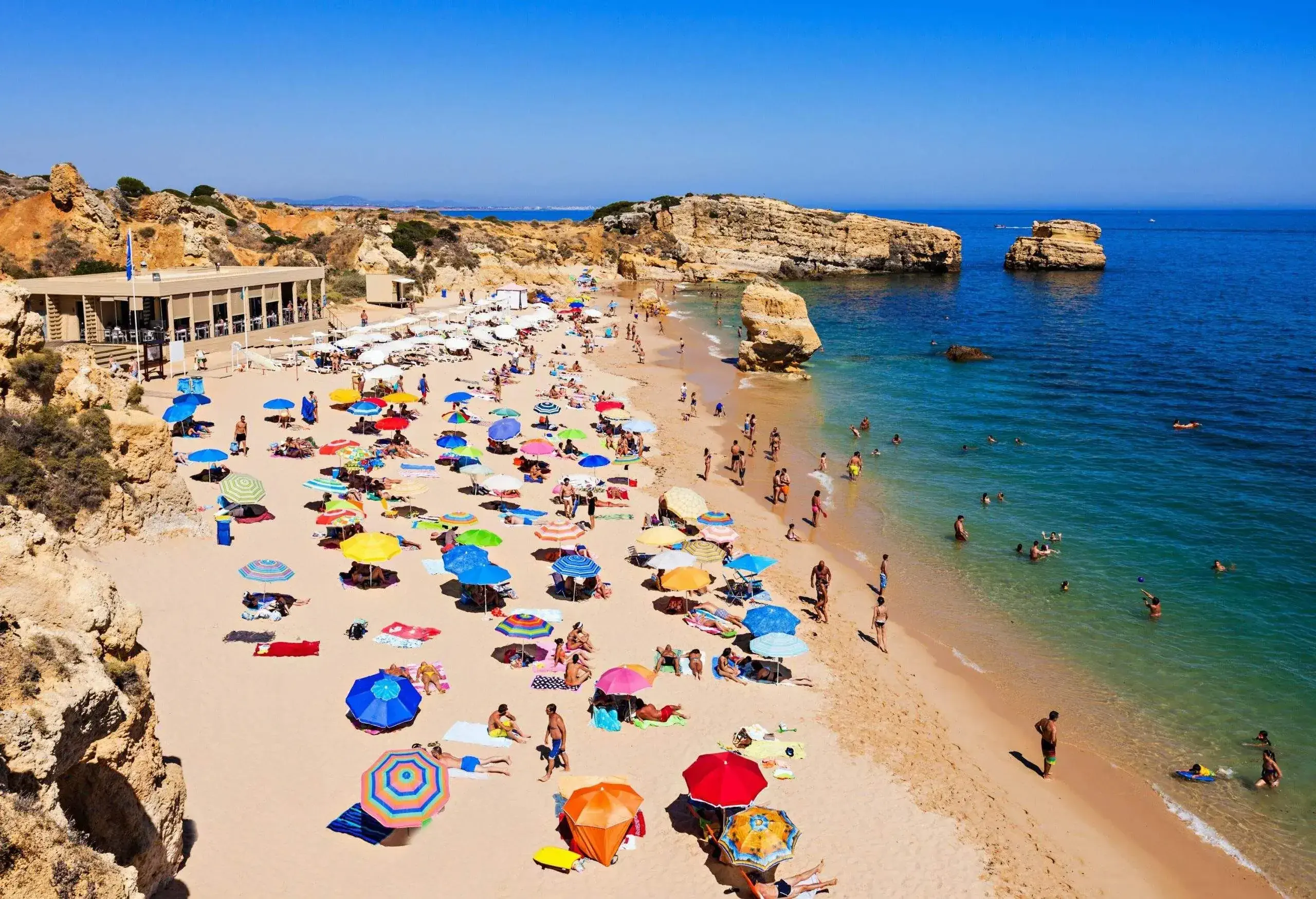 A balmy day on the beach with people playing in the water and relaxing on the sand under colourful umbrellas.