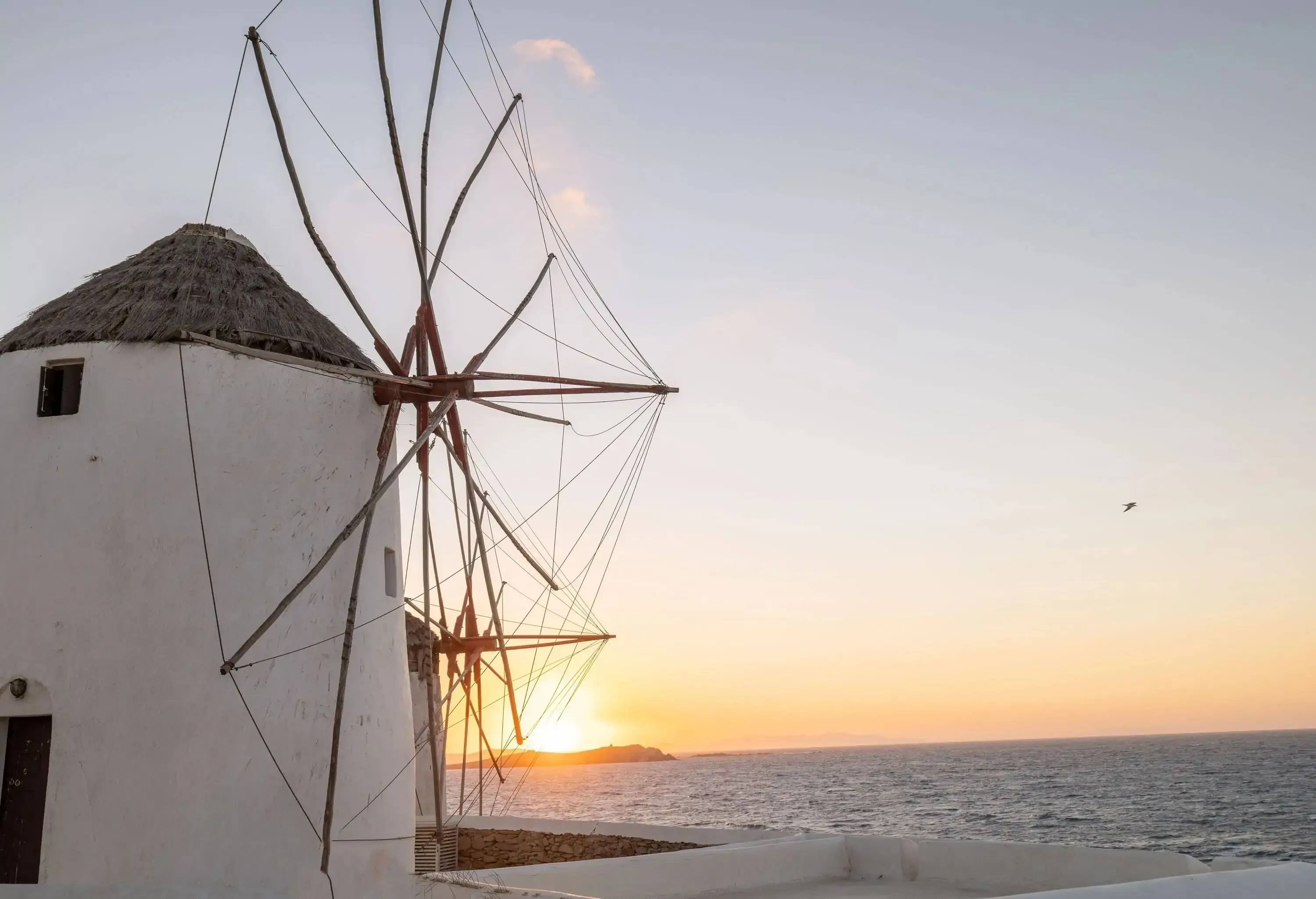 Mykonos' distinctive windmills with the sun setting over an island across the sea.