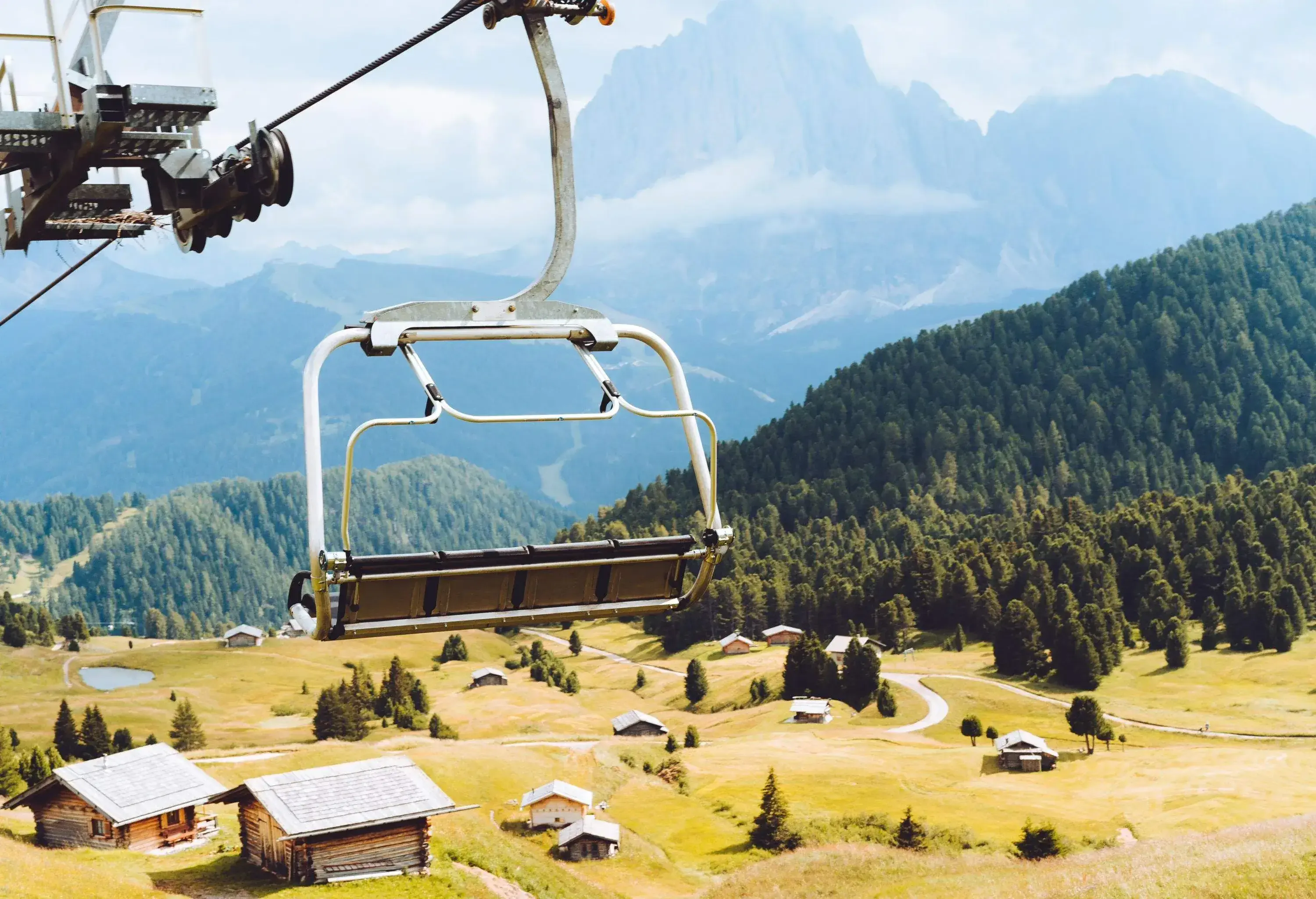 View from a chairlift in the Dolomites, with mountain range in background and pastures below