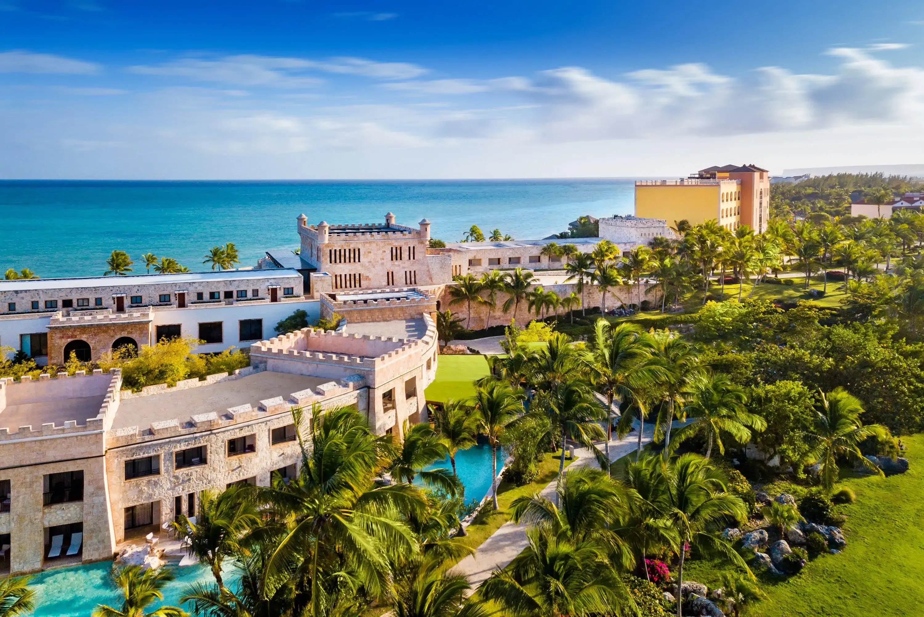 Aerial view of a luxury coastal resort with palm trees, pools, and the ocean.