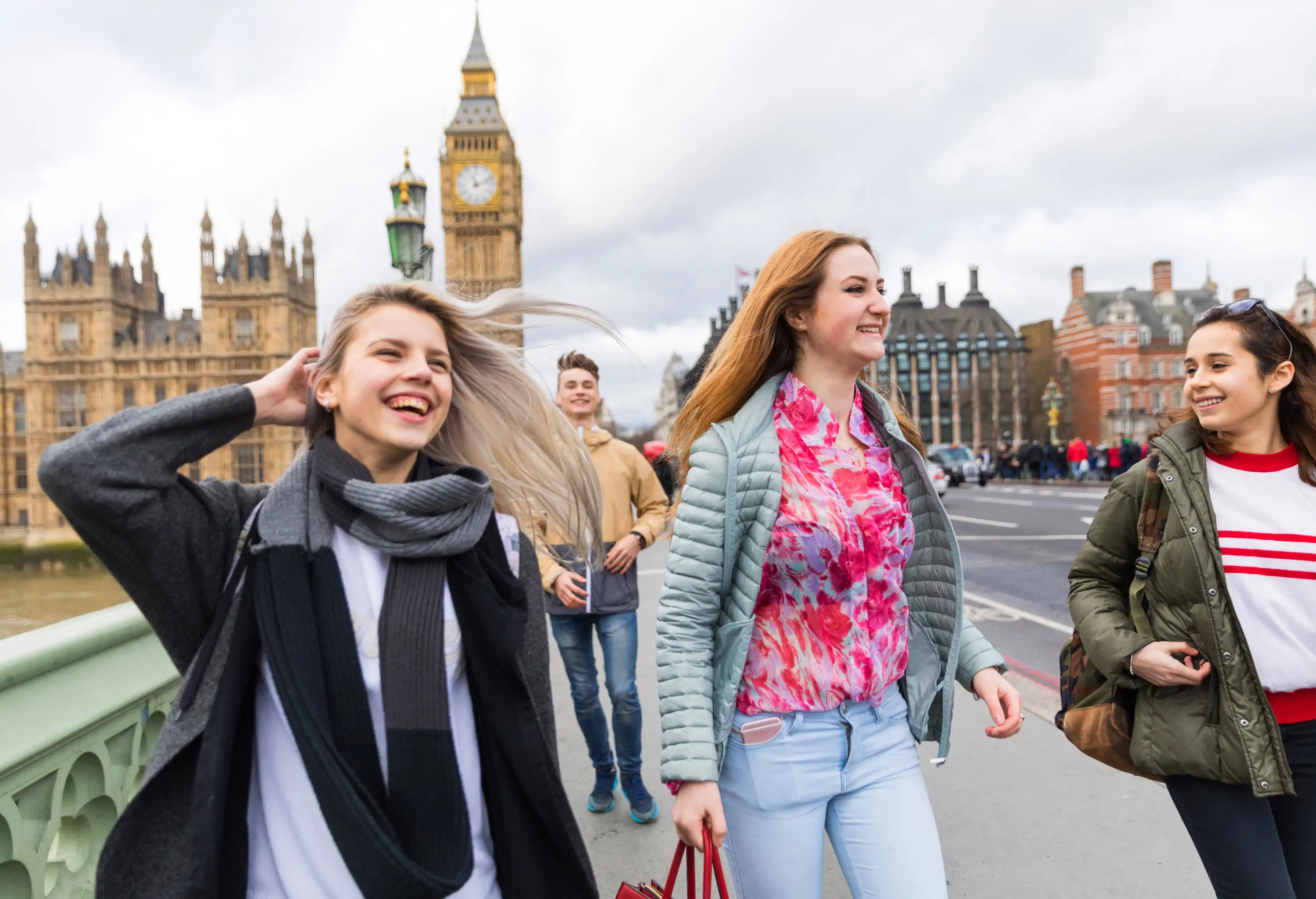 Four happy young individuals are on a bridge against the iconic Big Ben, a historic clock tower in London.