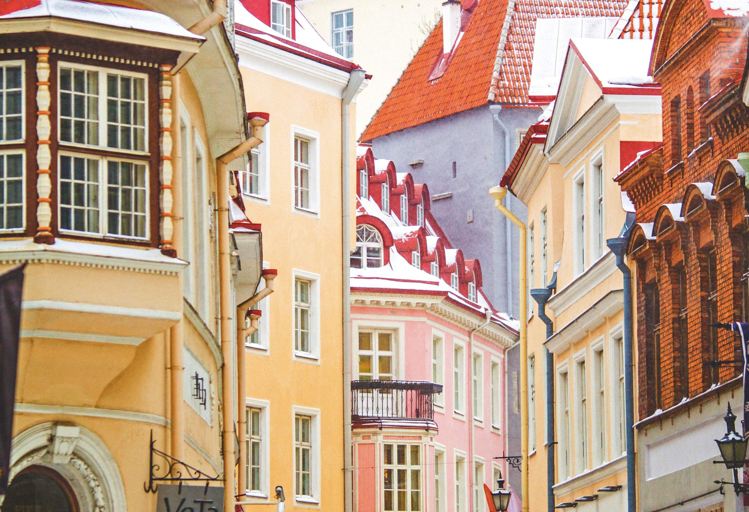 Two tourists walk on the snow-covered road between tall colourful buildings.