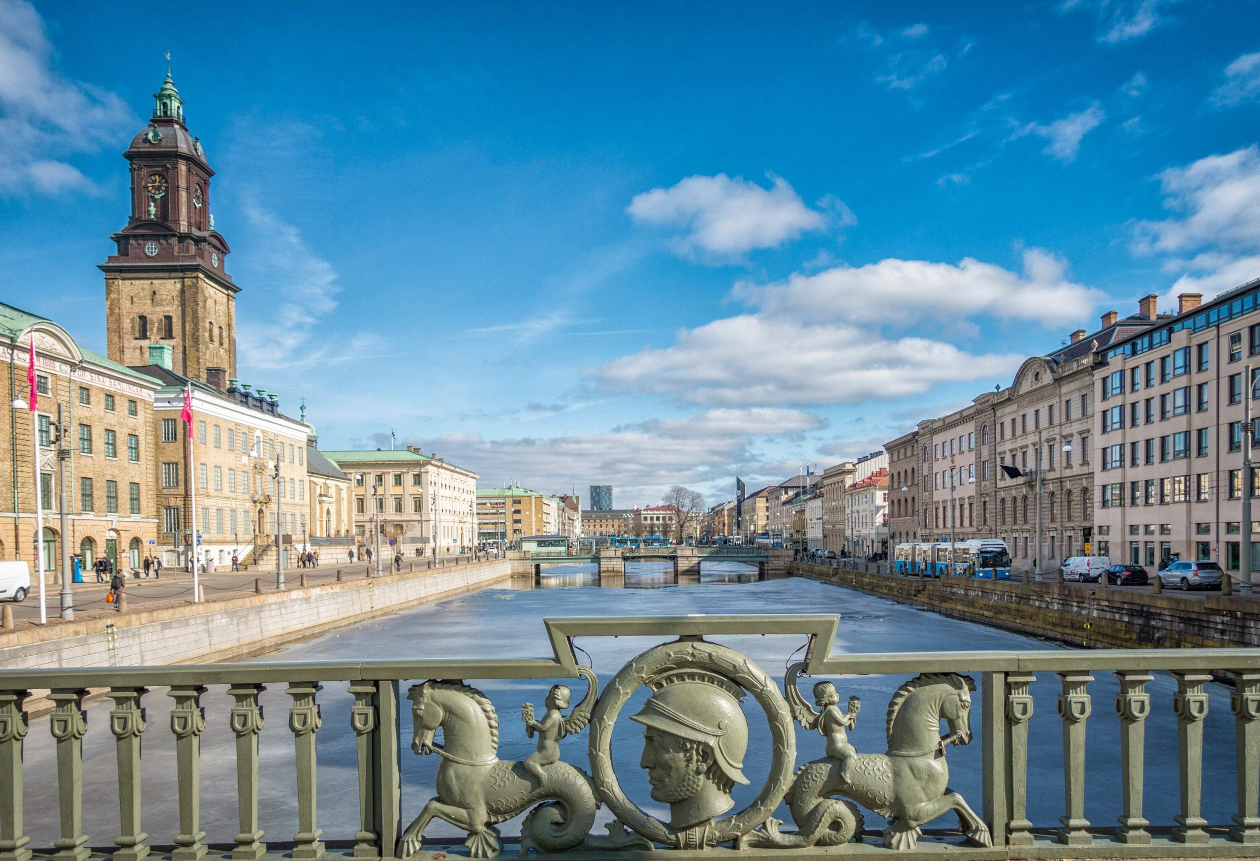 A canal lined with classic buildings with a Baroque clock tower against the blue sky seen from a bridge.