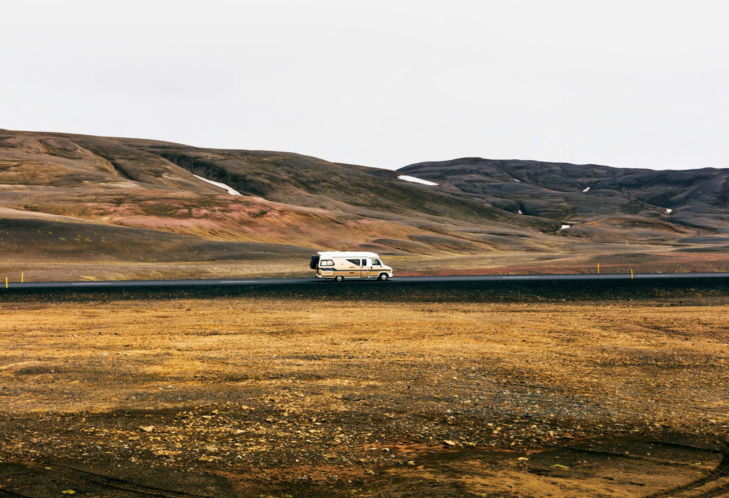 A motorhome travelling on a road between barren mountains and plains.