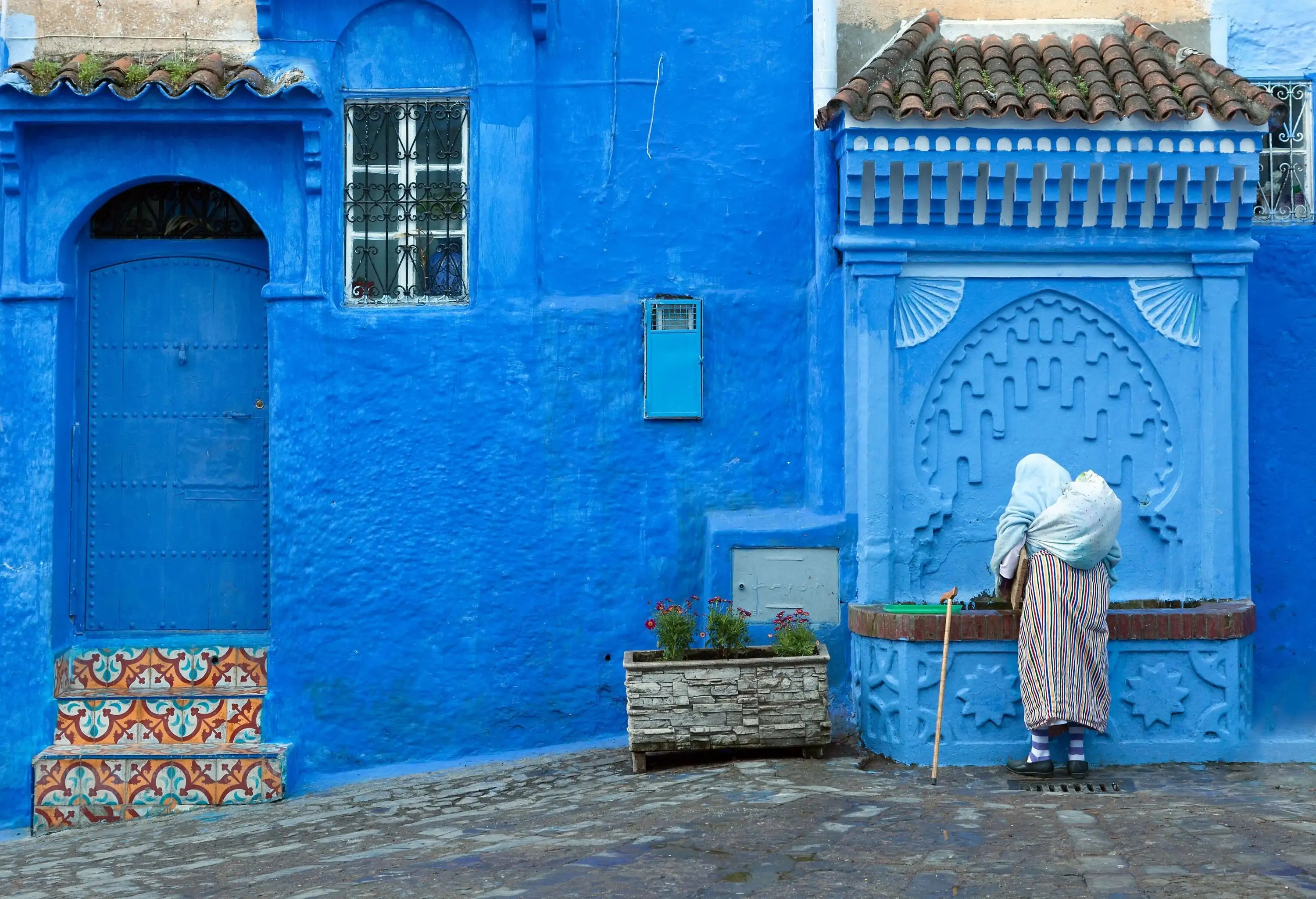 A person stands thoughtfully by a charming street, gazing upon a captivating row of buildings adorned in various shades of blue.