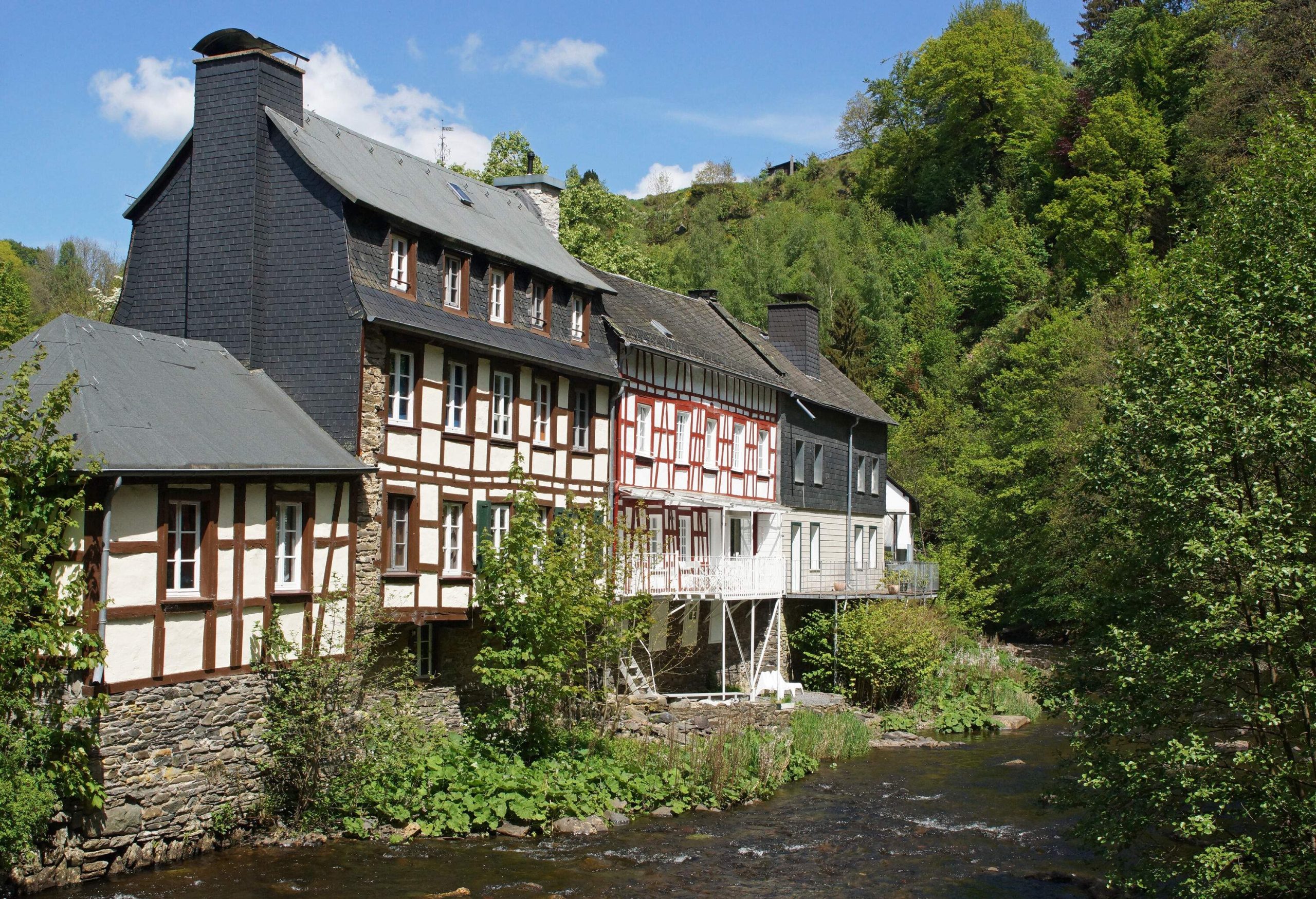 A shallow river flowing alongside timber-framed houses surrounded by trees.