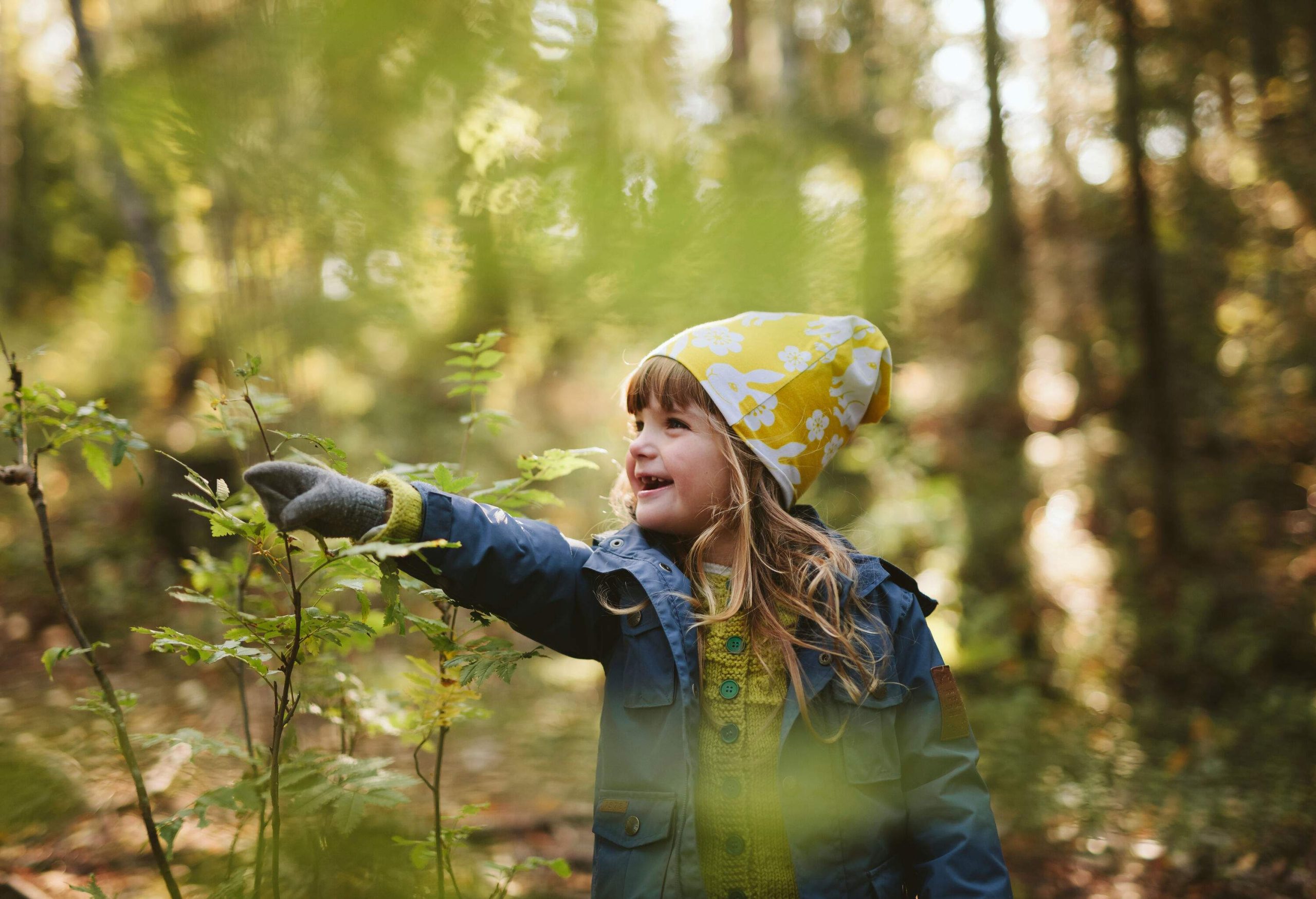 A little girl dressed in warm clothing pointing at a plant during forest hike.