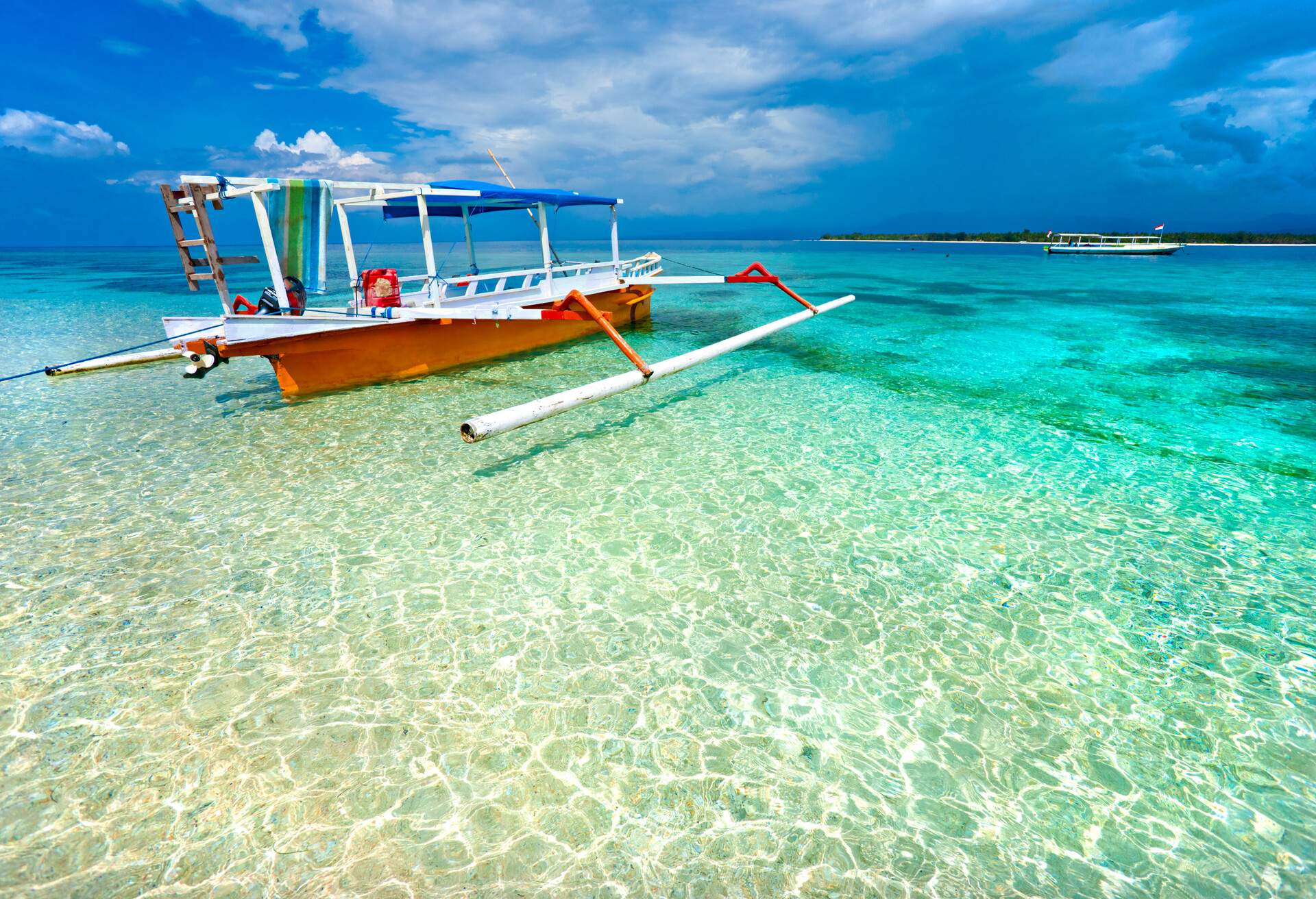 A stunning beach with a traditional double outrigger boat floating on crystal-clear waters.