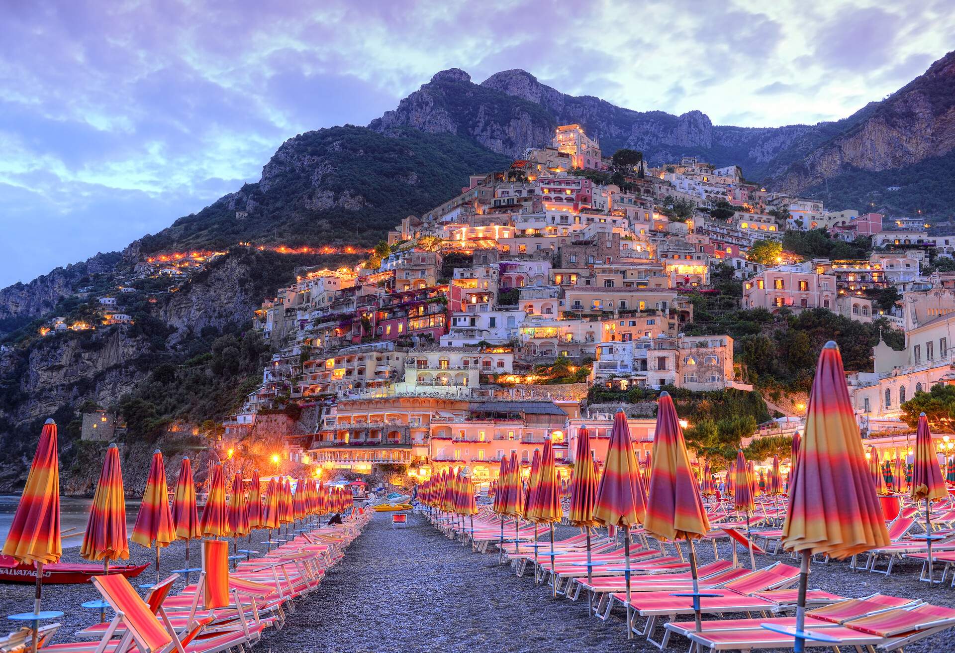 Illuminated, colourful, compact houses on the mountainside descend towards a beach packed with sunbeds and umbrellas.
