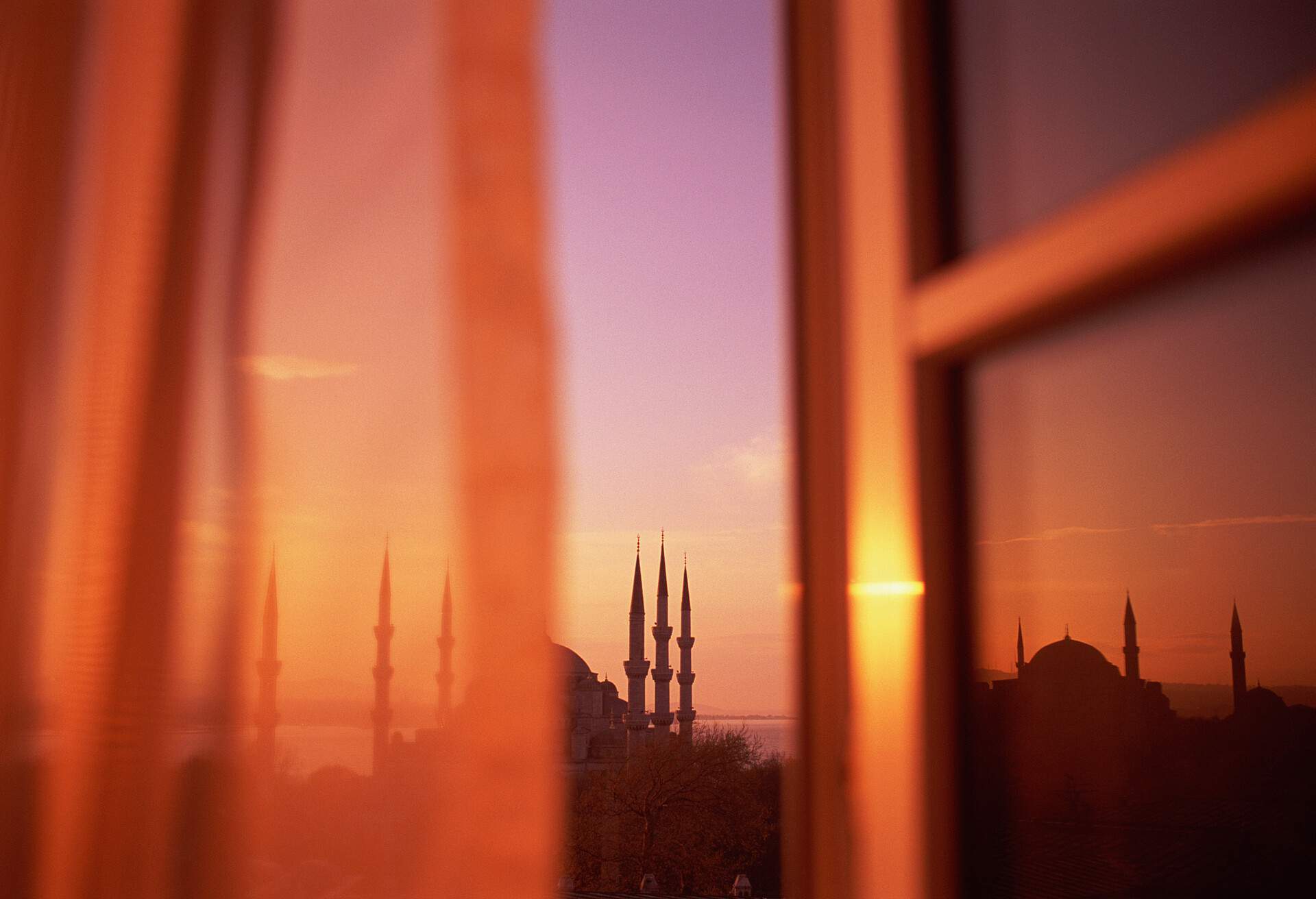 From a window hidden by a flowing curtain, a spectacular sight of the great Blue Mosque, with its remarkable domed top and soaring minarets.