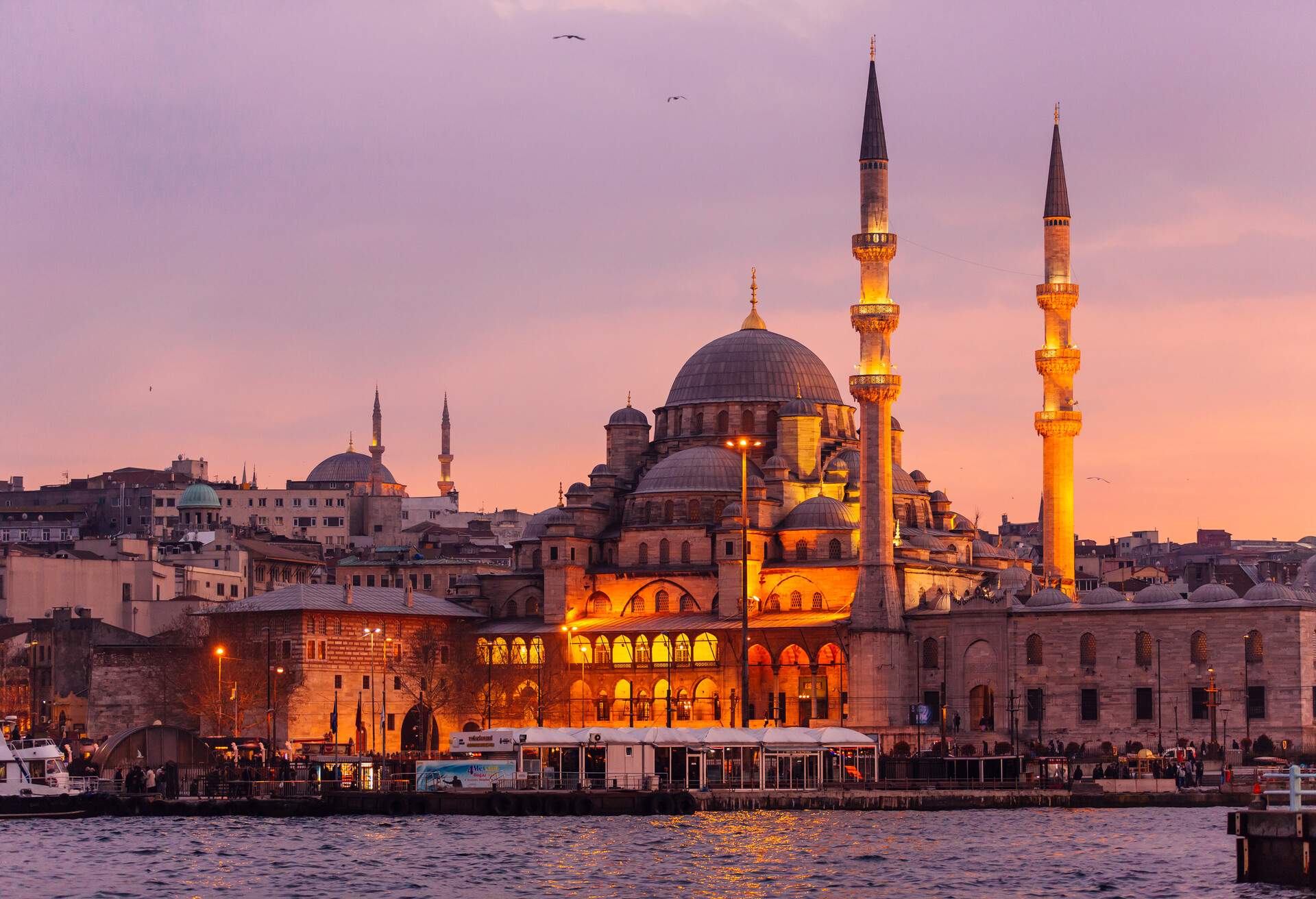 The luminous Yeni Cami and its towering minarets against a purple sky at dusk.