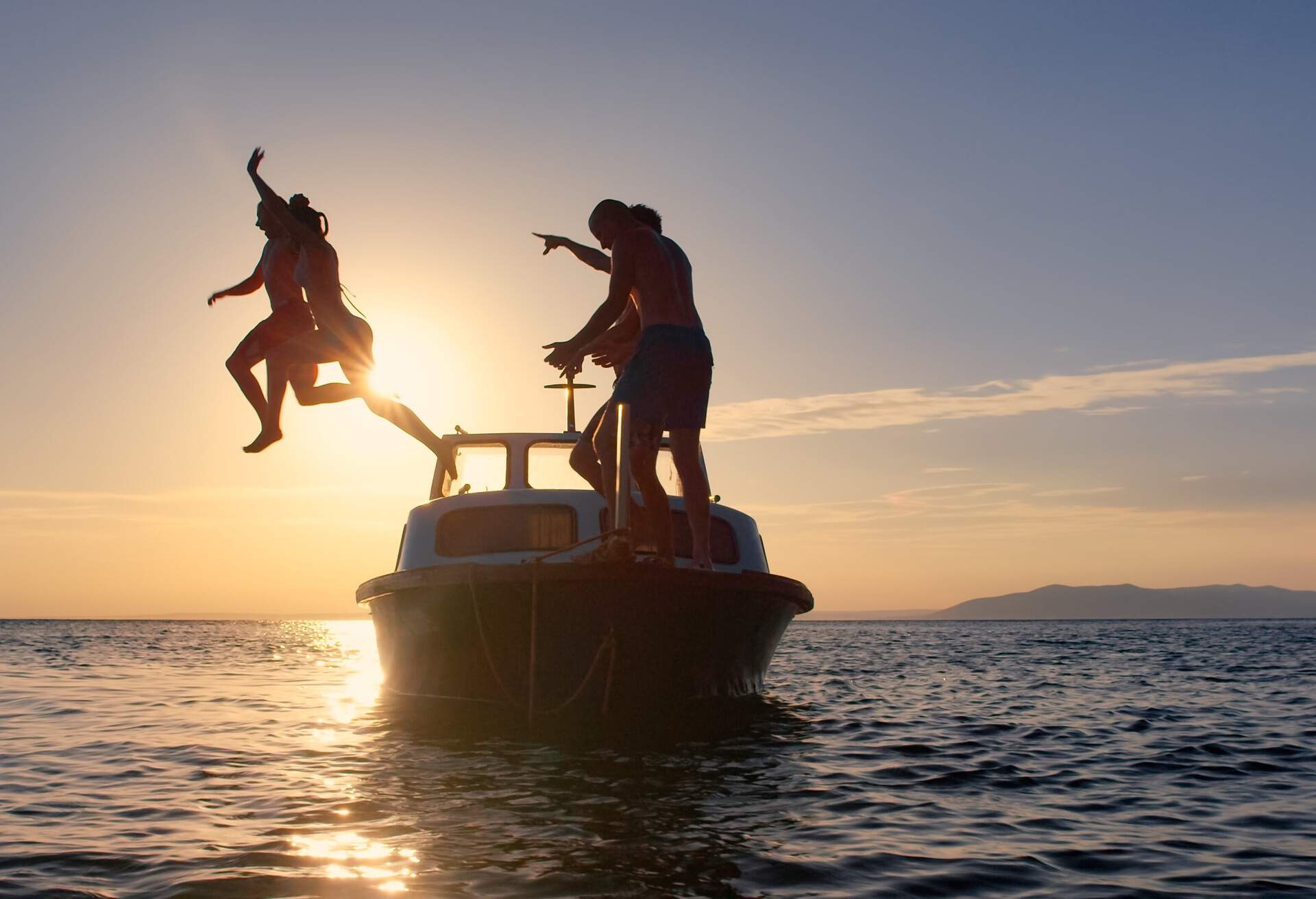 Friends diving into water from motorboat during sunset.