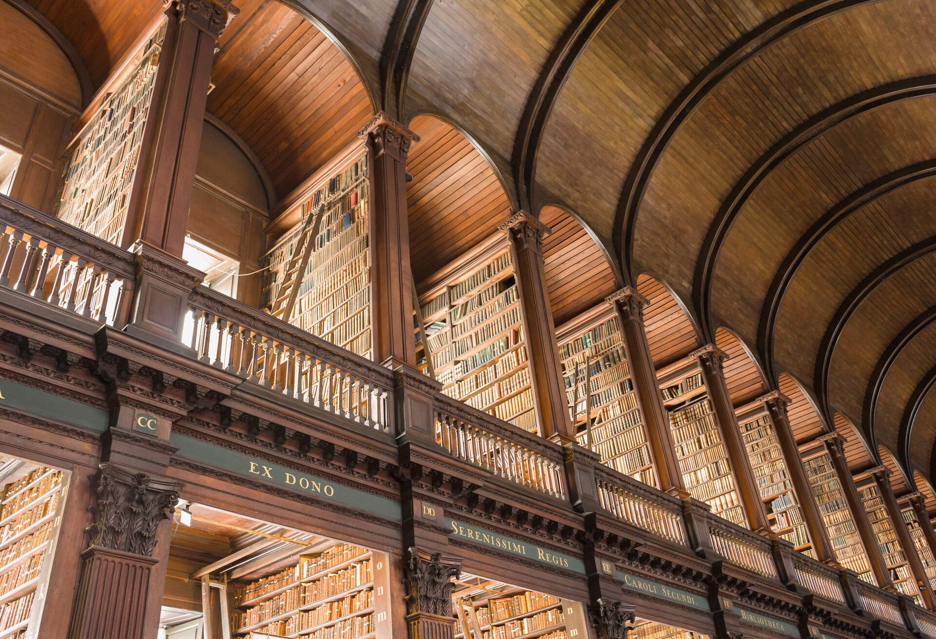 A library's top arcade with book-filled wooden shelves and rolling ladders.