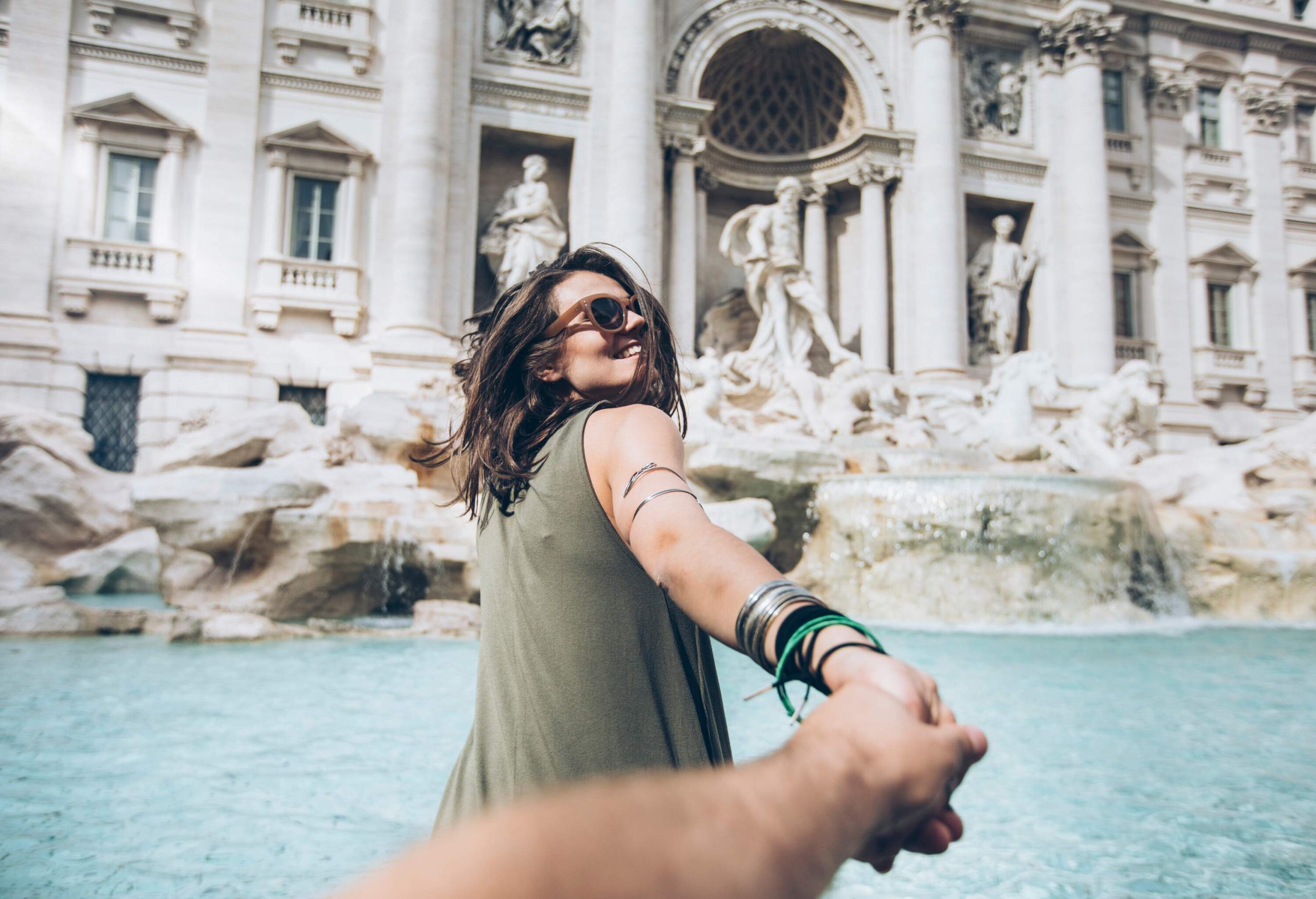 A woman in sunglasses smiles and glances back as she holds someone's hand.